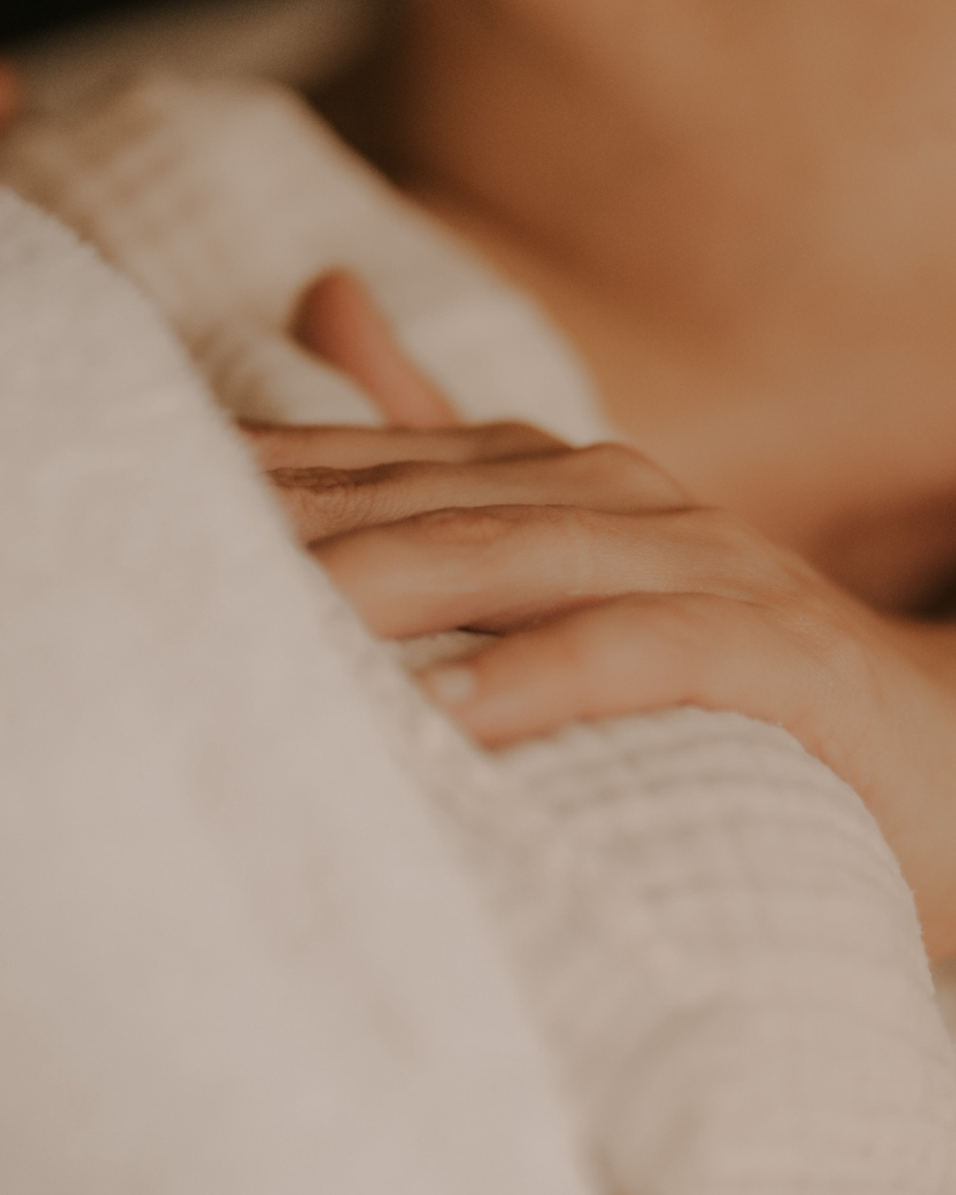 Close-up of a person's hand resting on a white towel or blanket, with part of the person's body partially visible in the background.
