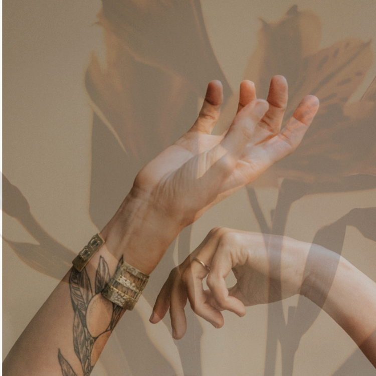 Close-up of two hands, one with tattoos, jewelry, and a watch, with fingers gesturing in the air, against a blurred floral background.