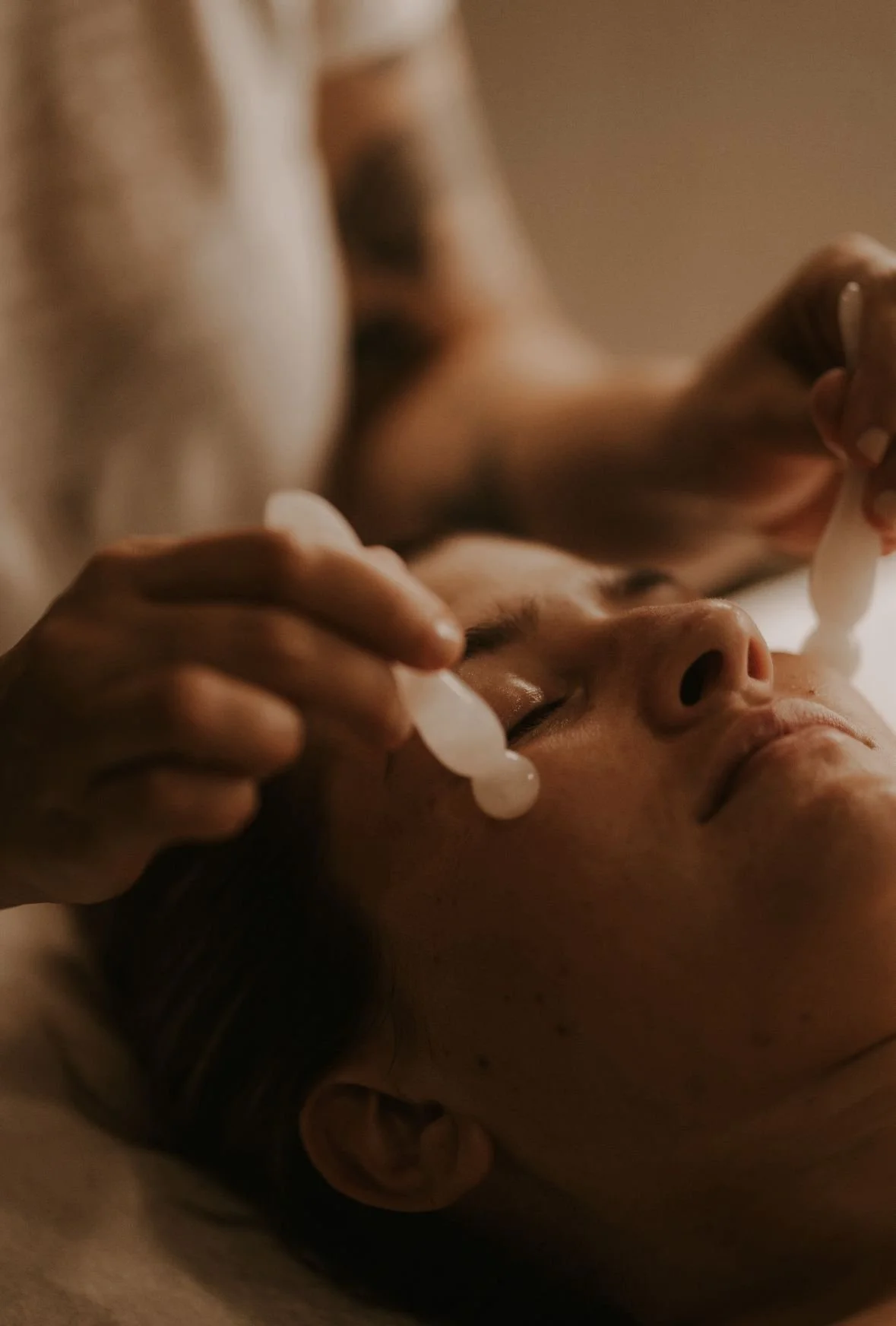 Person receiving a facial massage with skincare tools.