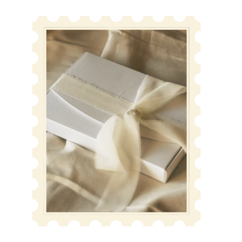 A white gift box with a satin ribbon bow, resting on cream-colored fabric.