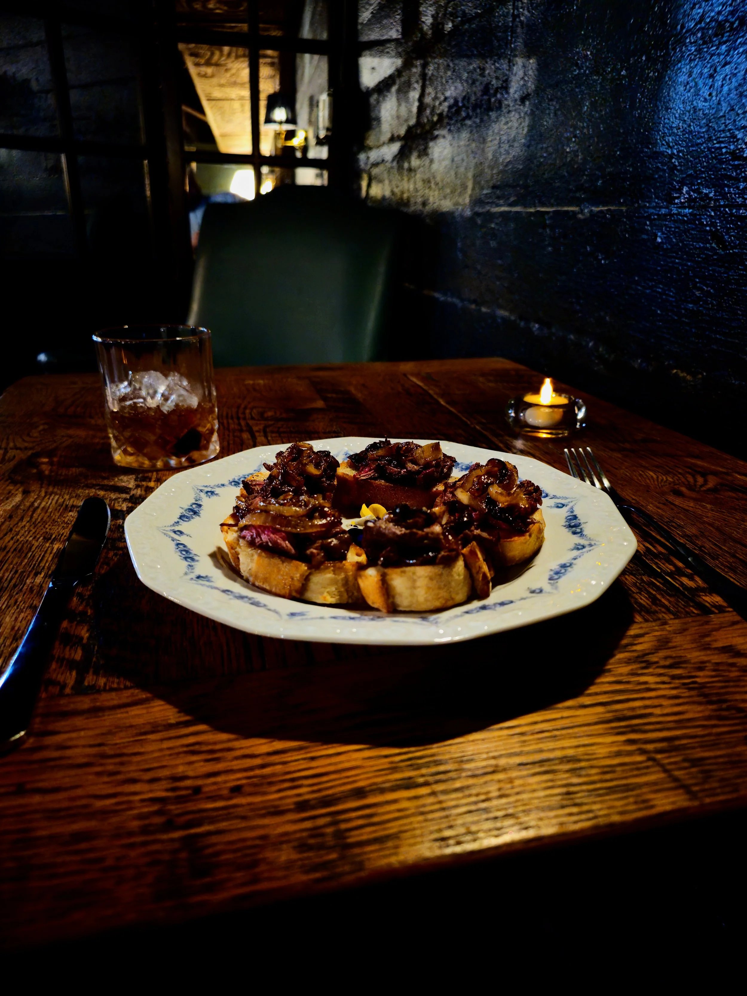 Steak Crostinis with cocktail in background and low lighting.