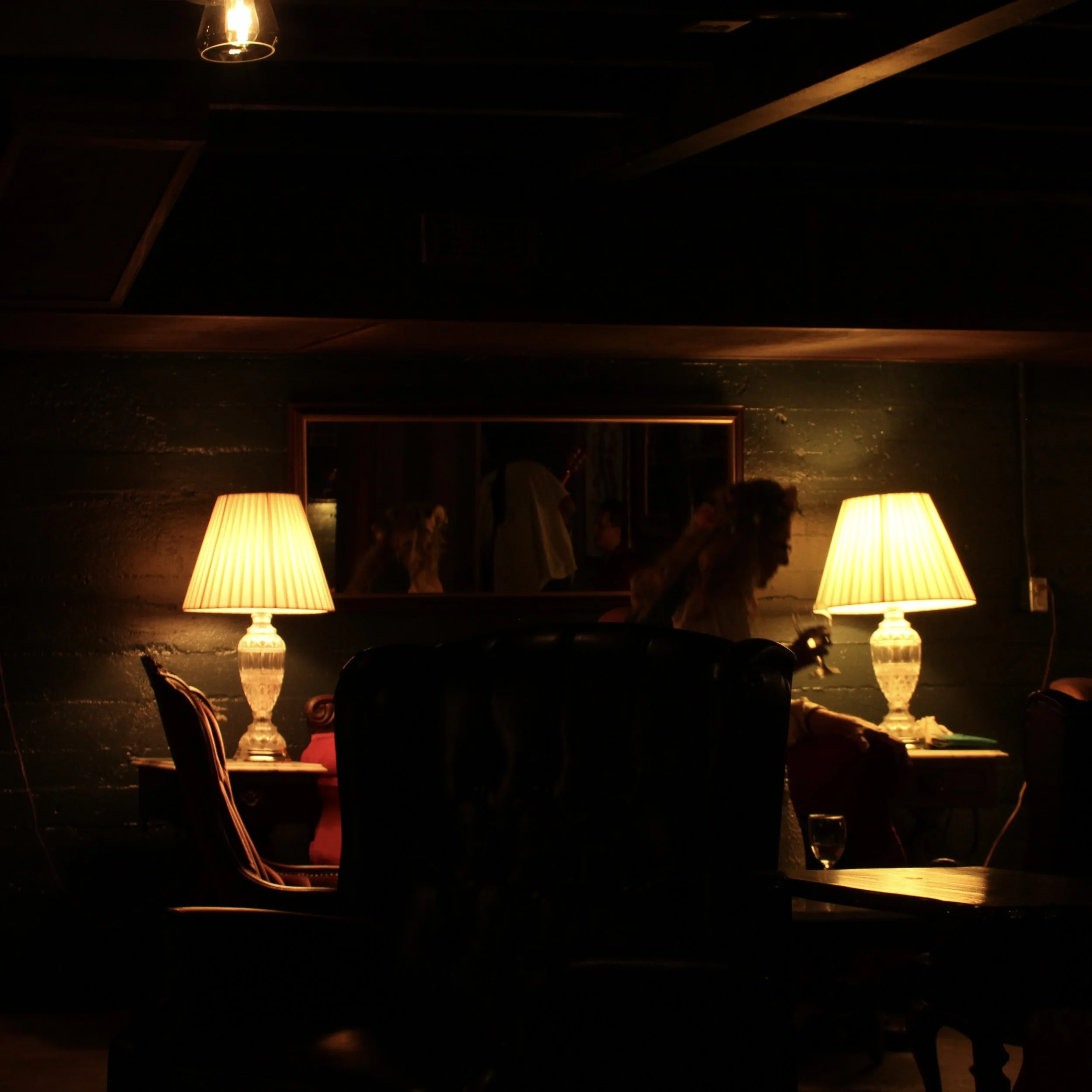 Dimly lit room with two table lamps casting warm light on surrounding furniture and walls, reflecting in a large mirror on the wall.
