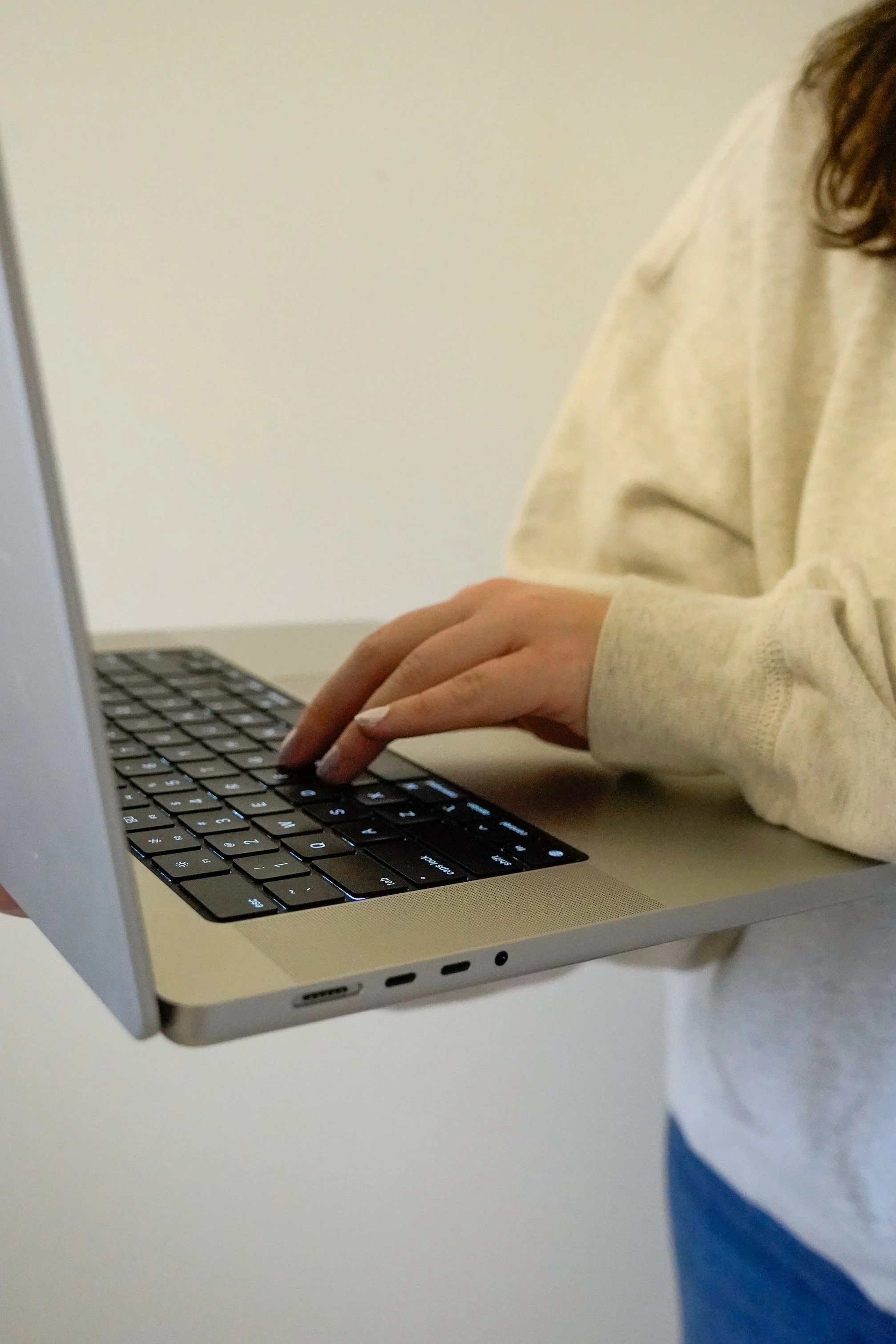 Person typing on a laptop keyboard wearing a beige sweatshirt.