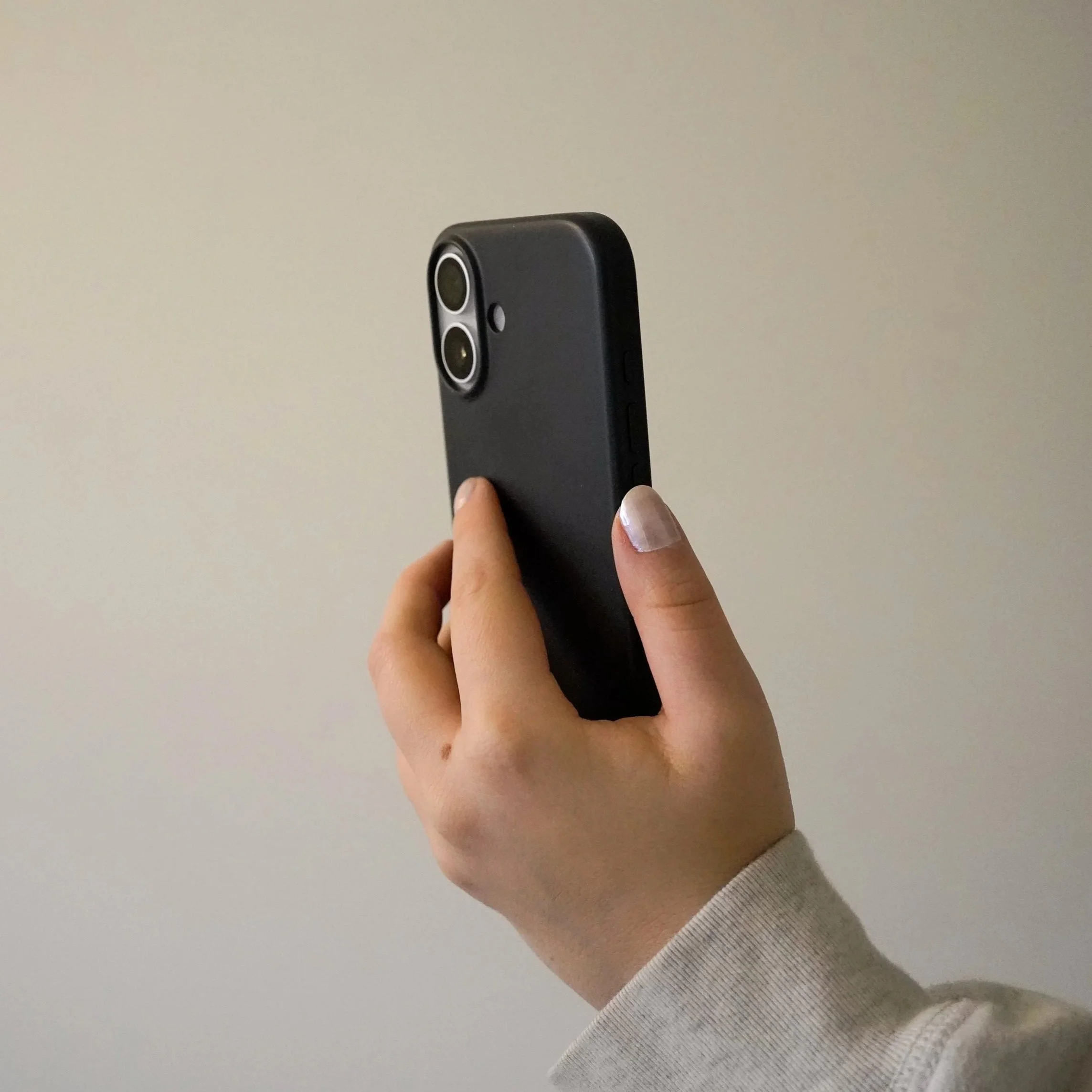 A hand holding a black smartphone with a dual camera setup against a plain, light-colored background.