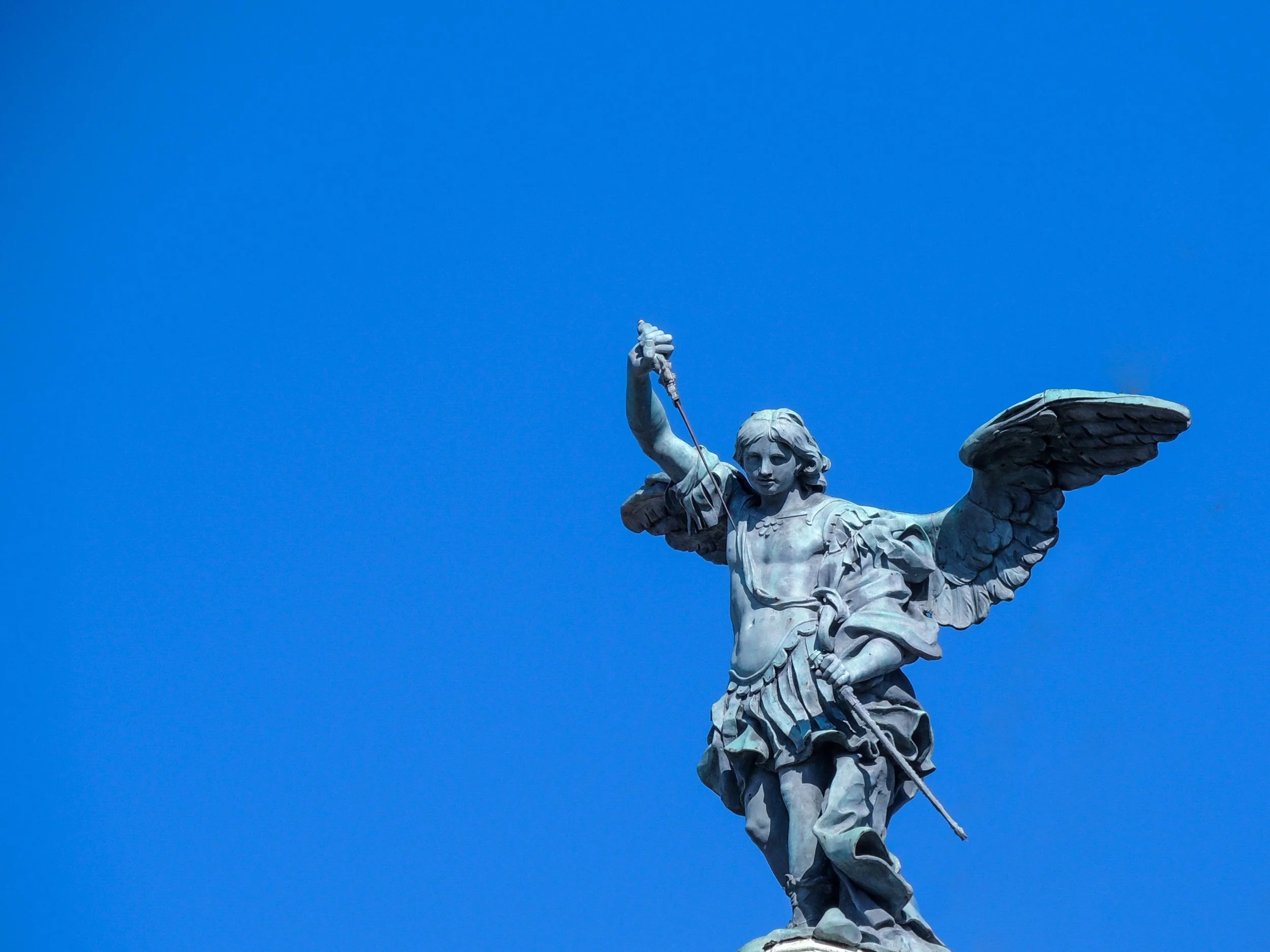 Close-up of a statue of an angel holding a sword, with a clear blue sky in the background.