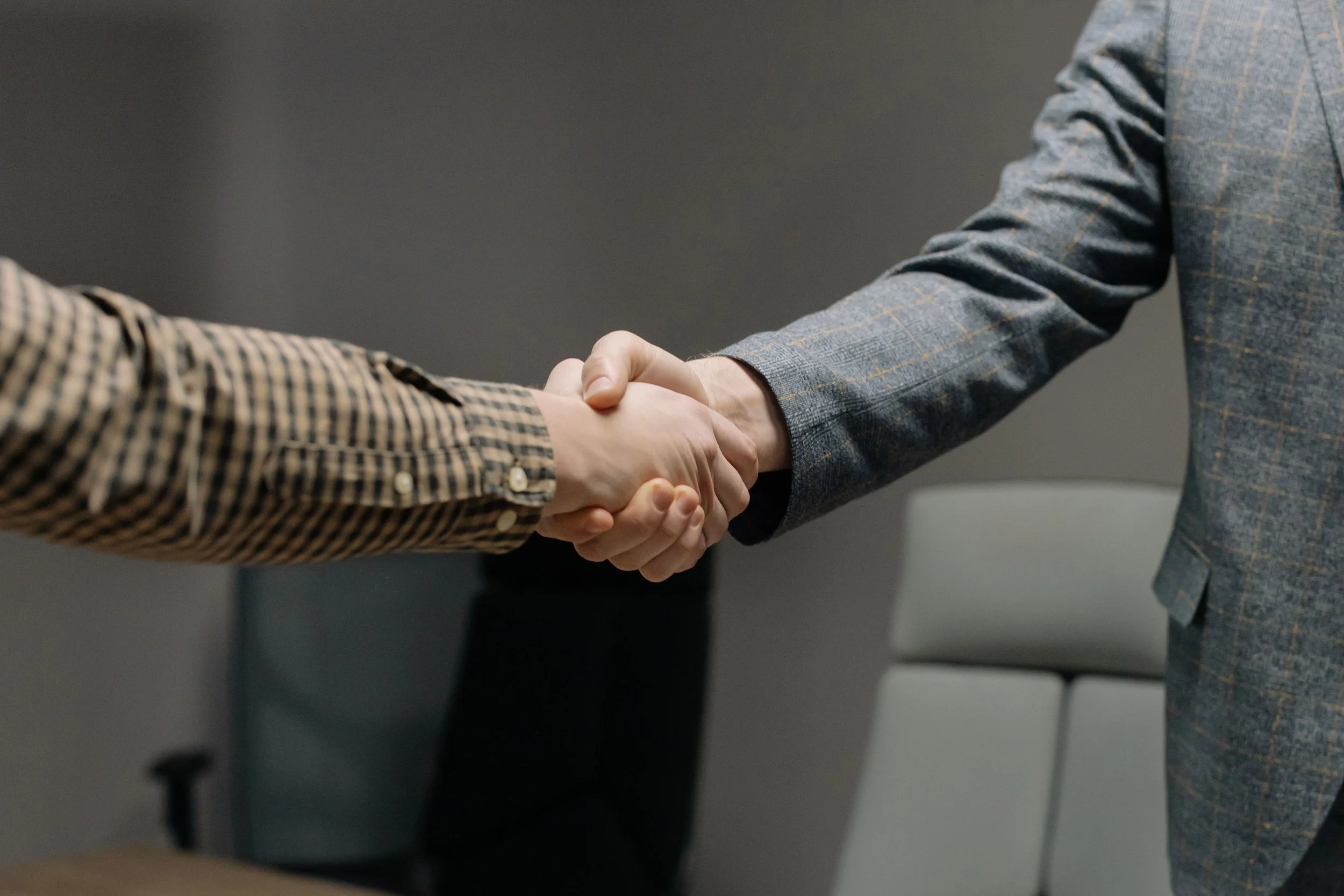 Two individuals in business attire shaking hands in an office or conference room setting.