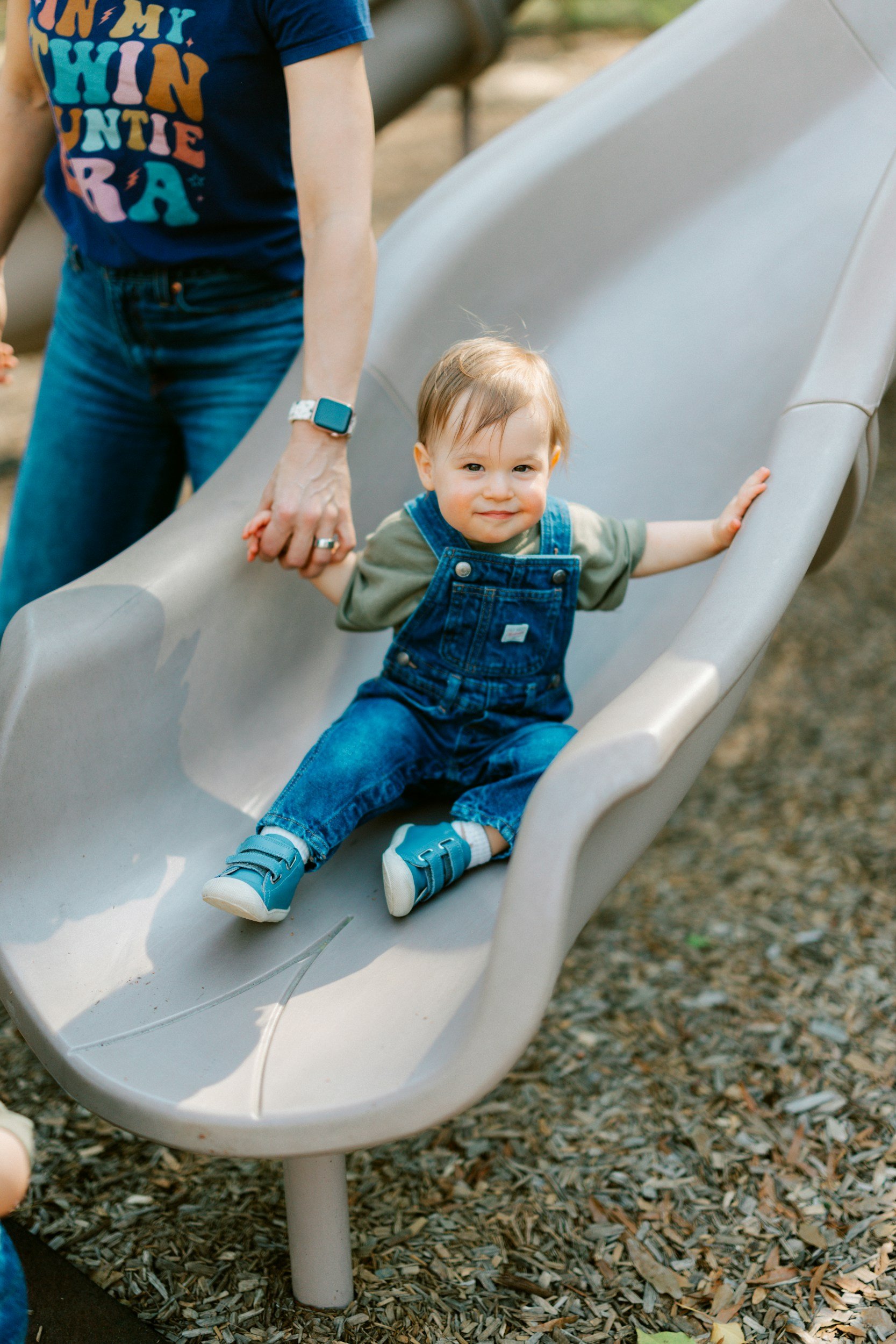Young child enjoying outdoor play at a playground while holding a caregiver’s hand, reflecting the safe, attentive childcare provided by Balanced Babysitting.