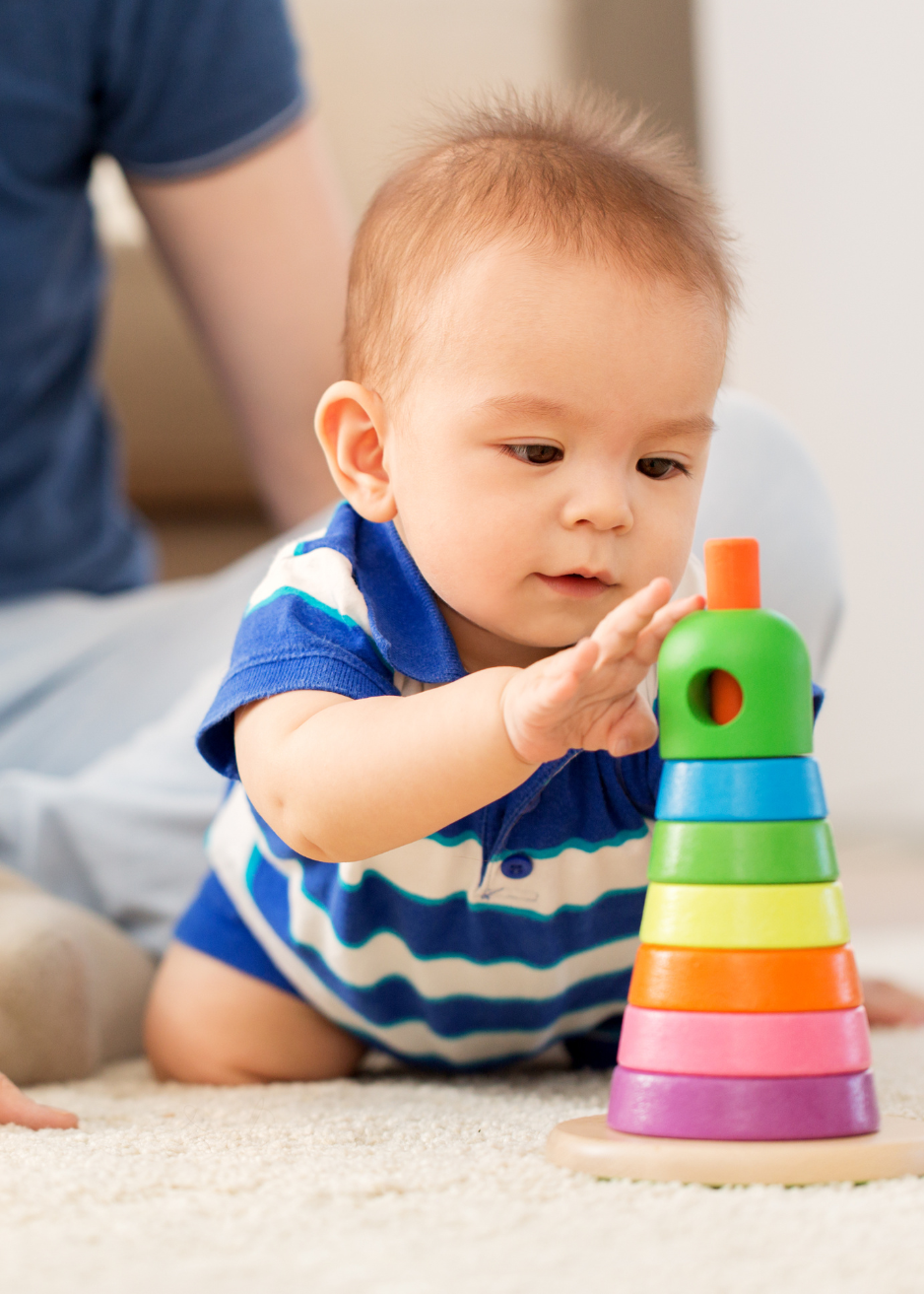 Young child developing fine motor skills and problem-solving abilities through hands-on play with colorful stacking toys in a safe, nurturing environment.