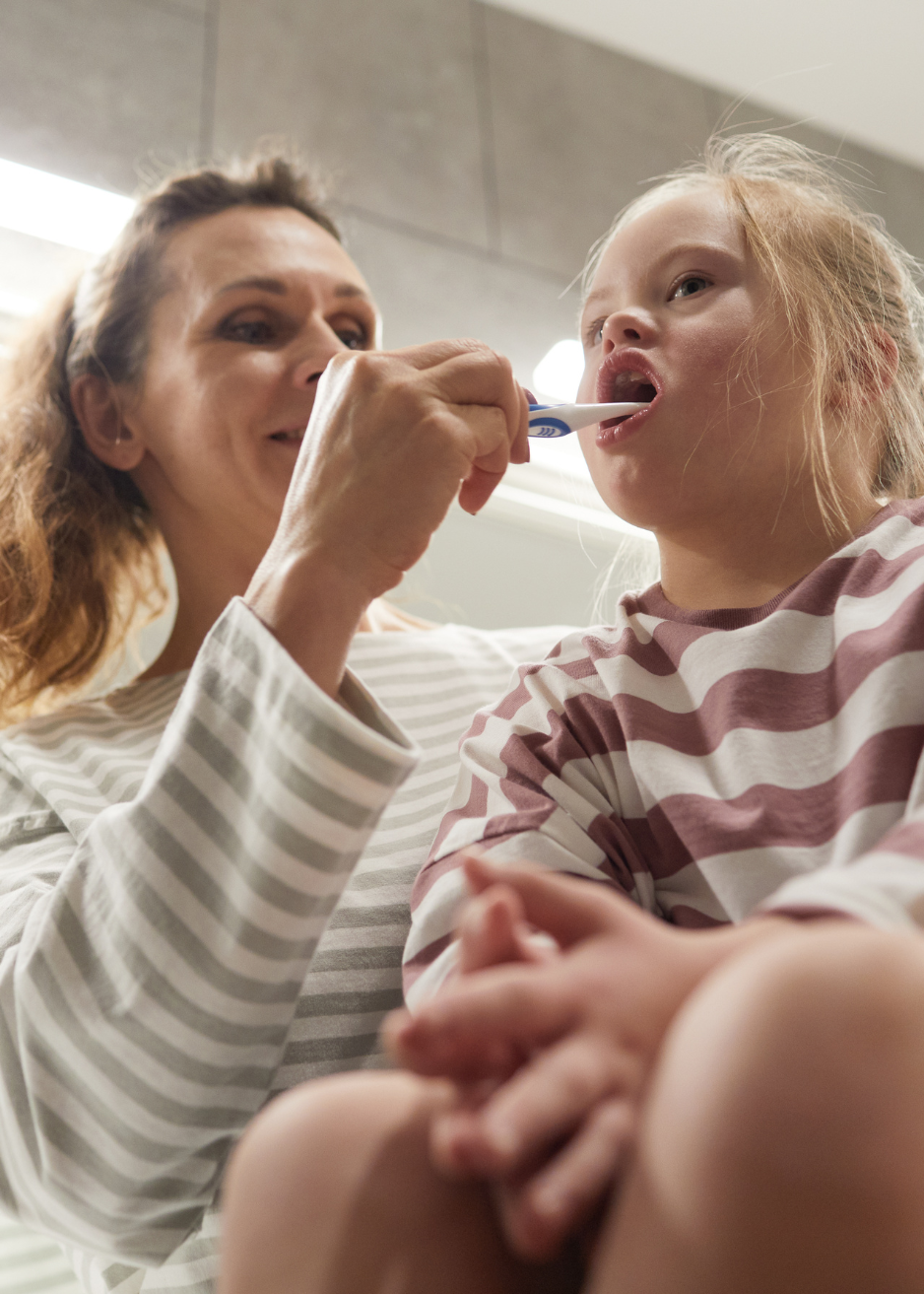 Caregiver helping a young child brush her teeth, supporting healthy routines, independence, and daily care in a safe and nurturing environment.