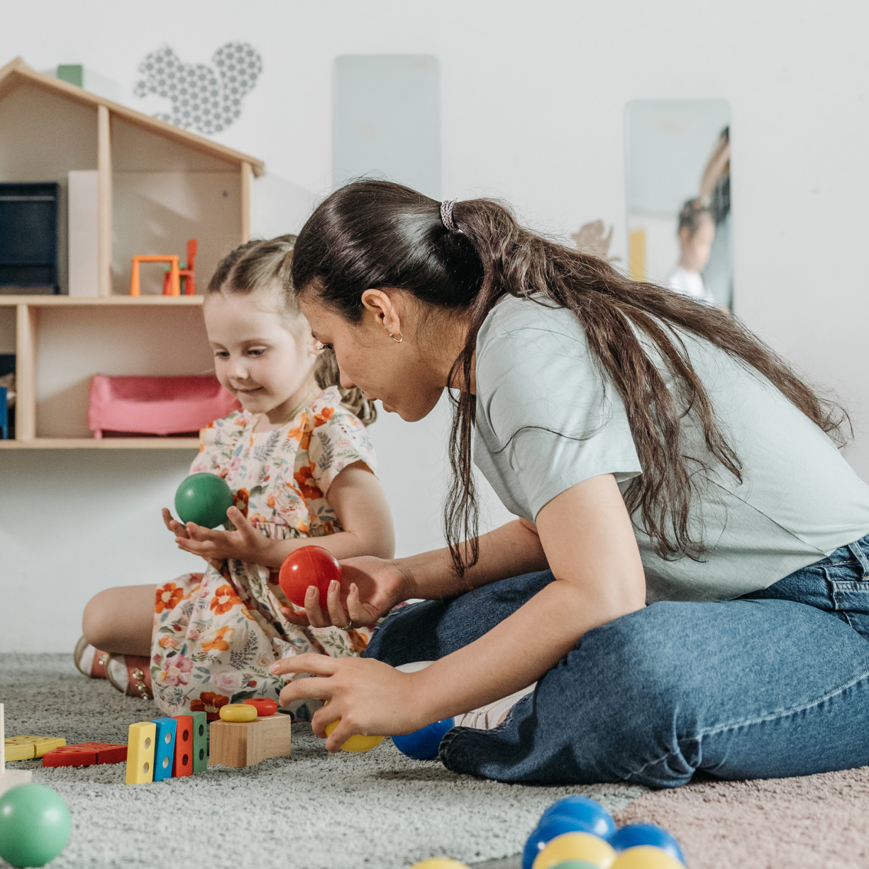 Caregiver and child enjoying hands-on play with colorful toys, fostering creativity, learning, and meaningful connections for Main Line and Chester County families.