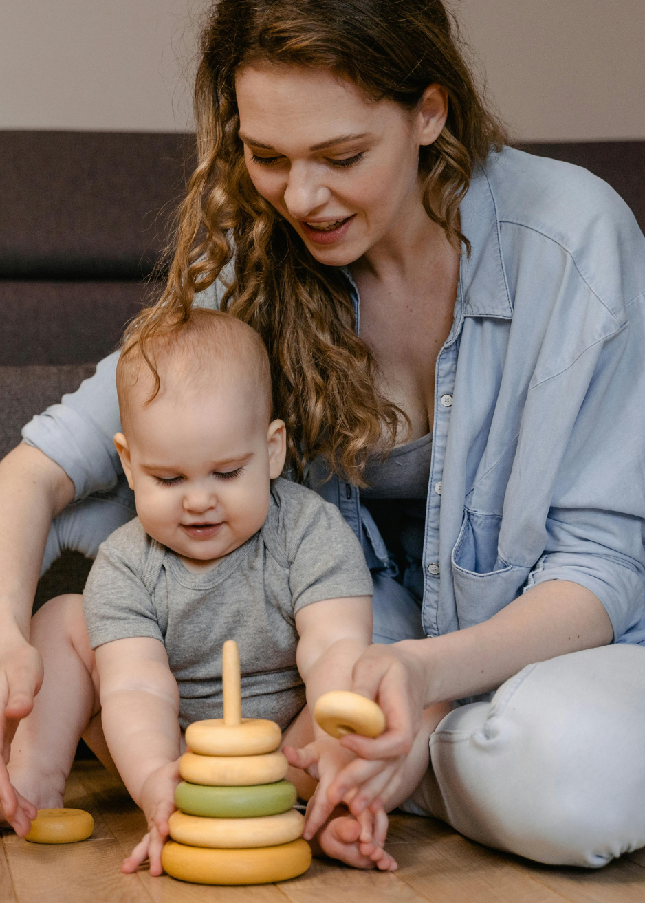 Caregiver and young child engaged in developmental play with a wooden stacking toy, supporting learning, creativity, and connection for families in the Main Line and Chester County, PA.