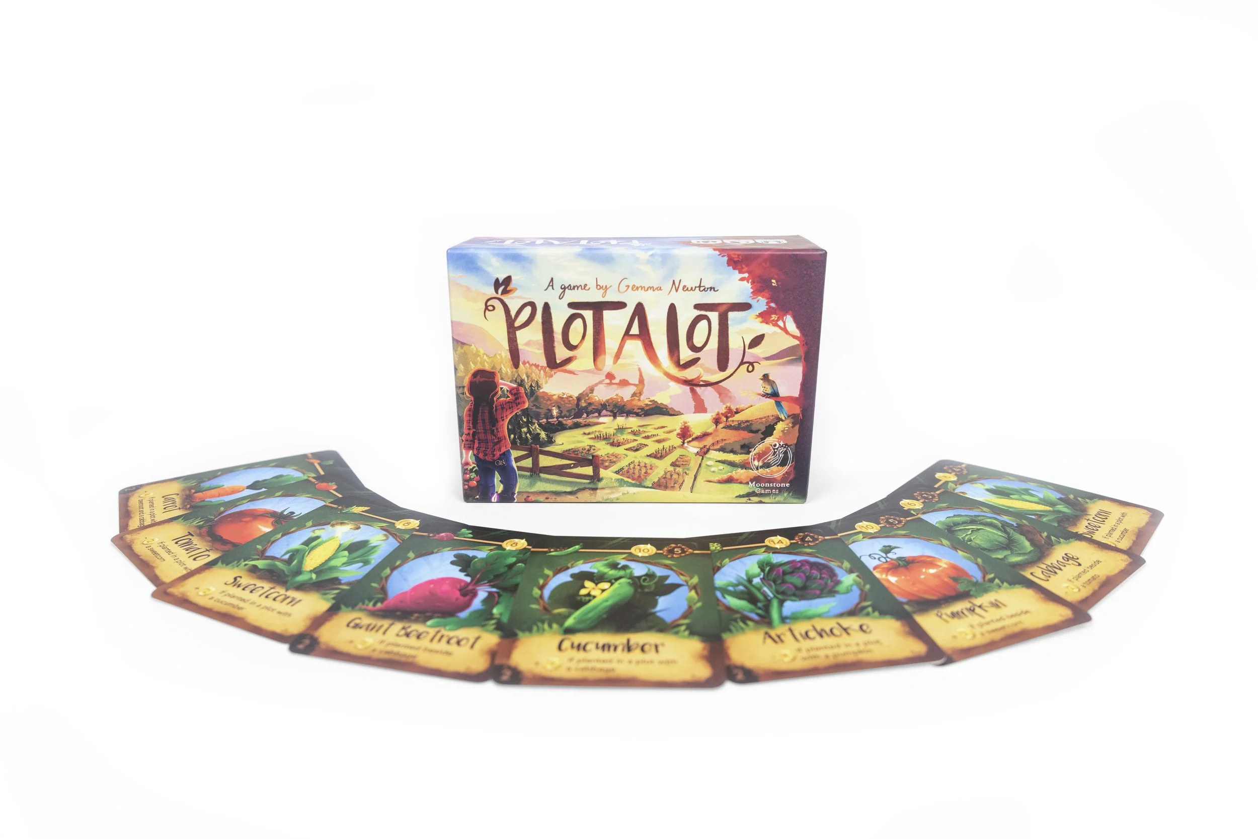 Board game titled "Plotalot" with colorful illustrated box and game cards depicting vegetables laid out in a fan shape.