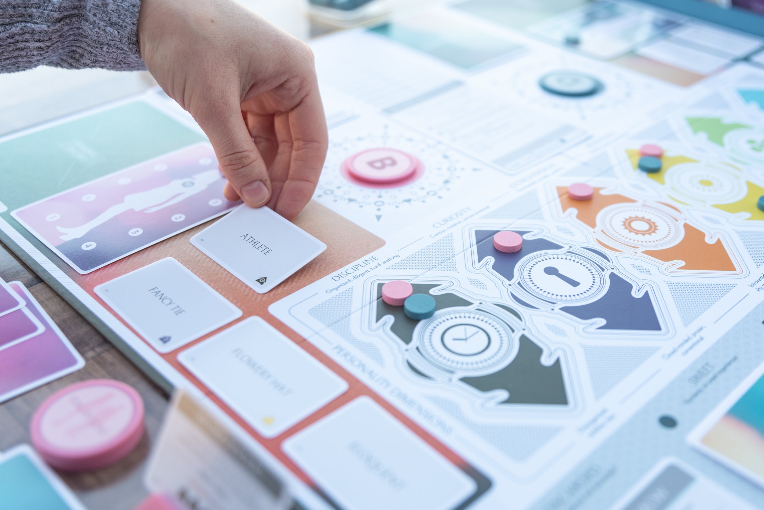 A person placing a card labeled 'Athlete' on a colorful board game with various tokens and game pieces.