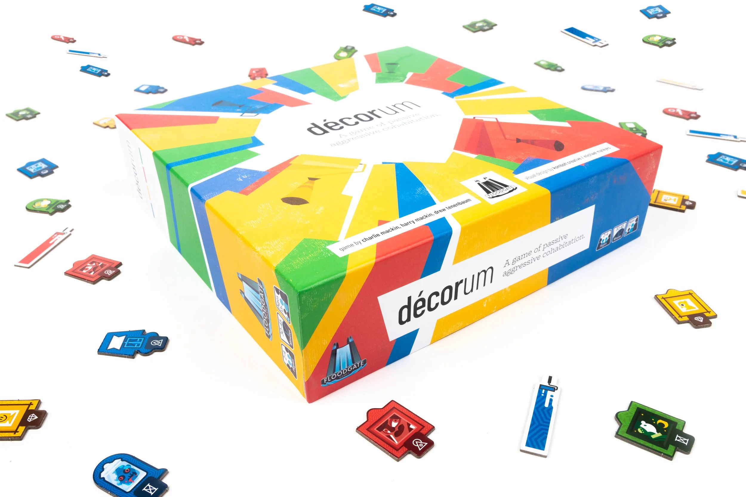 Colorful board game box labeled 'décorum' on a white surface with scattered game pieces around it.