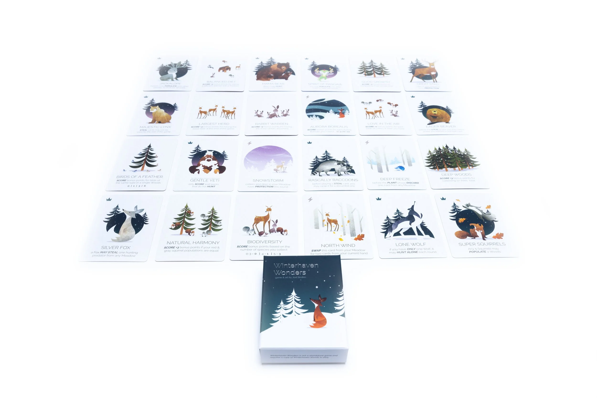 A card game called 'Winterhaven Woods' with multiple illustrated cards depicting winter animals and themes, arranged on a white surface, with the game box featuring a fox sitting under snow-covered trees.
