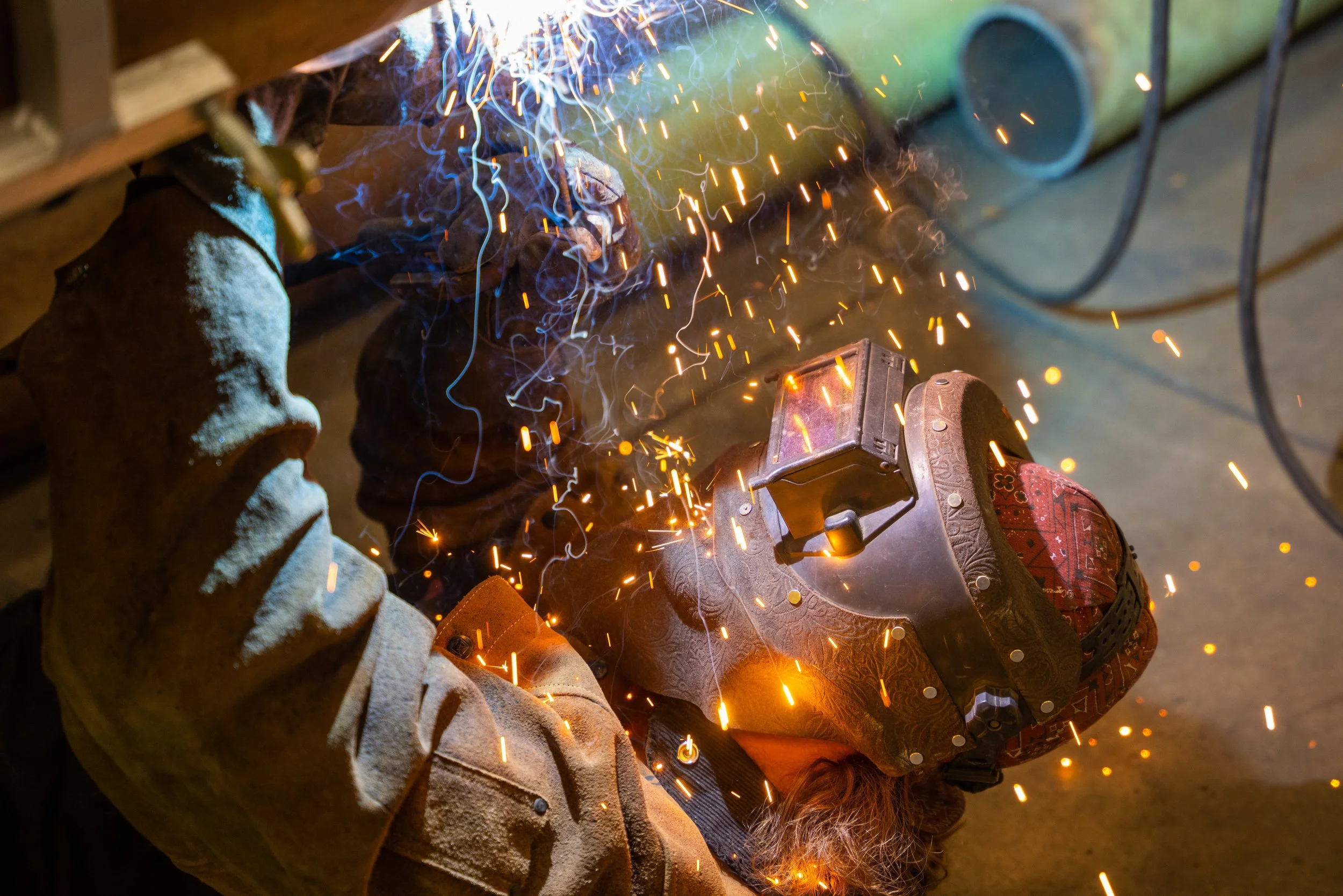 A person welding metal, sparks flying in various directions, wearing protective gear including gloves and a helmet.