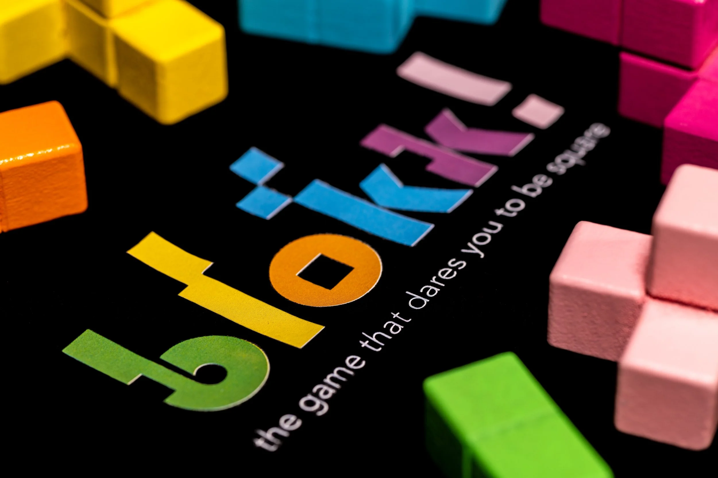 Close-up of colorful game pieces on a black board with the word 'blokk' and the phrase 'the game that dares you to be brave'.