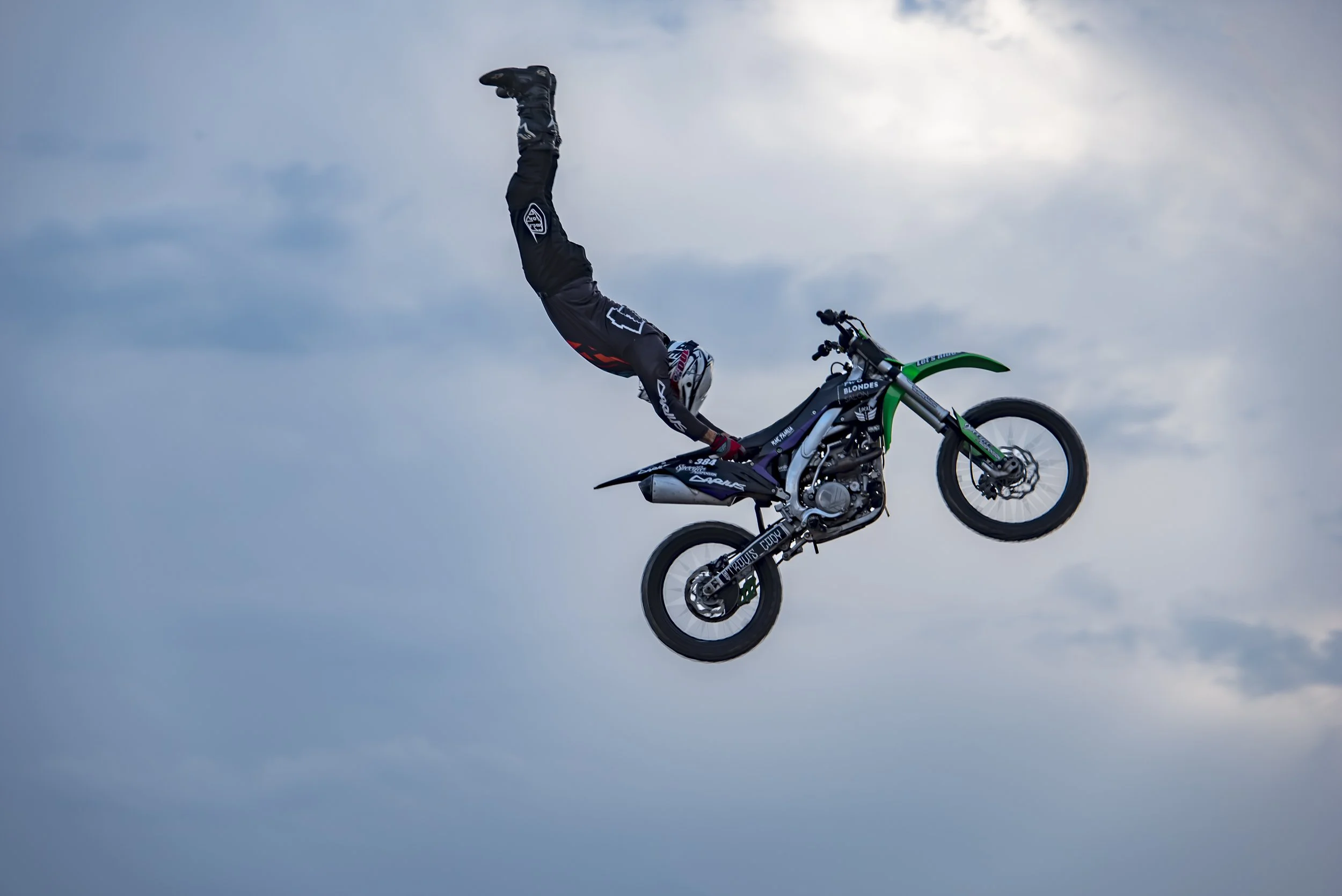 A motocross rider performing a stunt mid-air against a cloudy sky background.