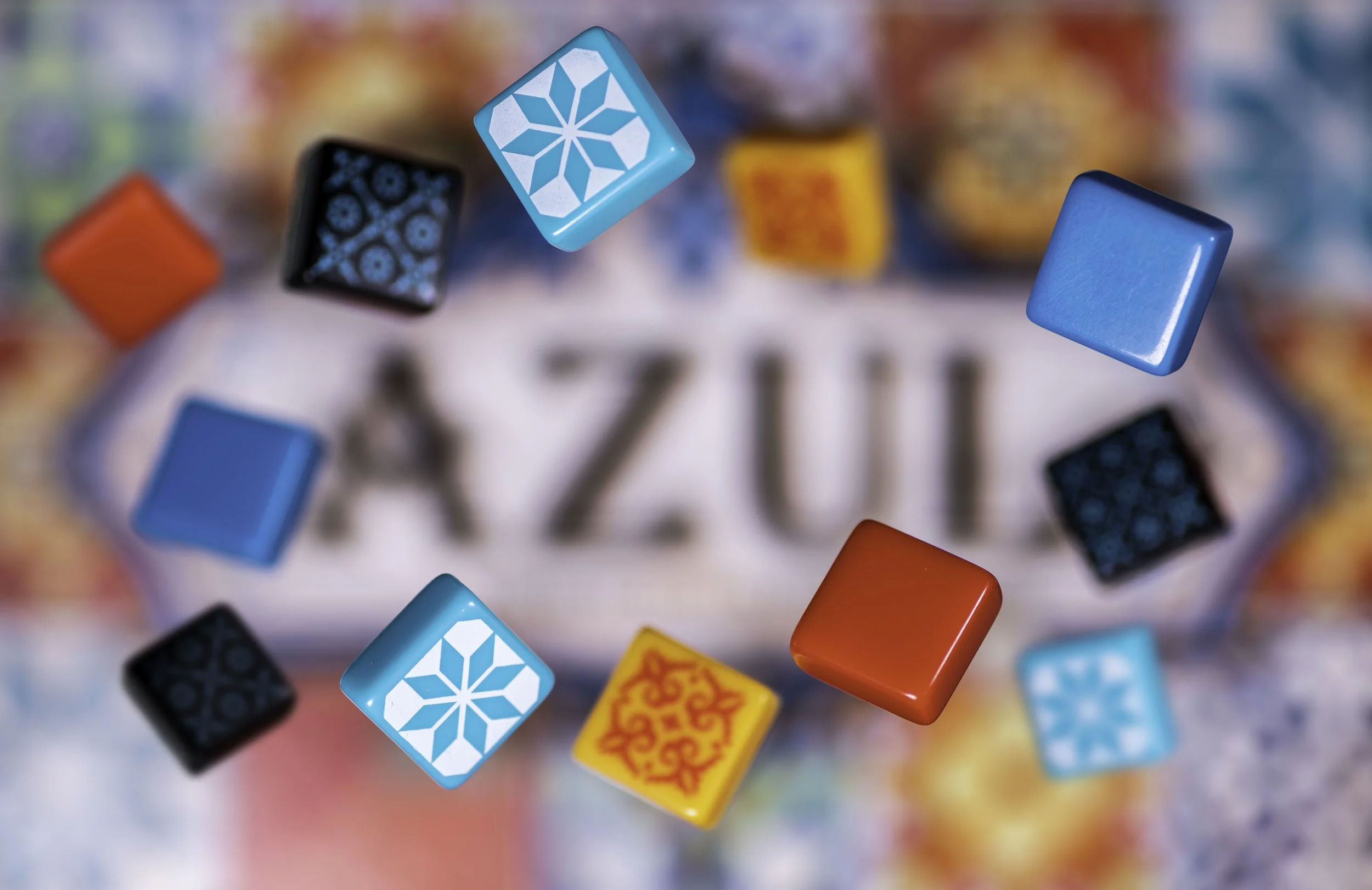 Close-up of colorful tiles and the word "Azul" on a blurred background, with game pieces featuring intricate patterns and vibrant colors.