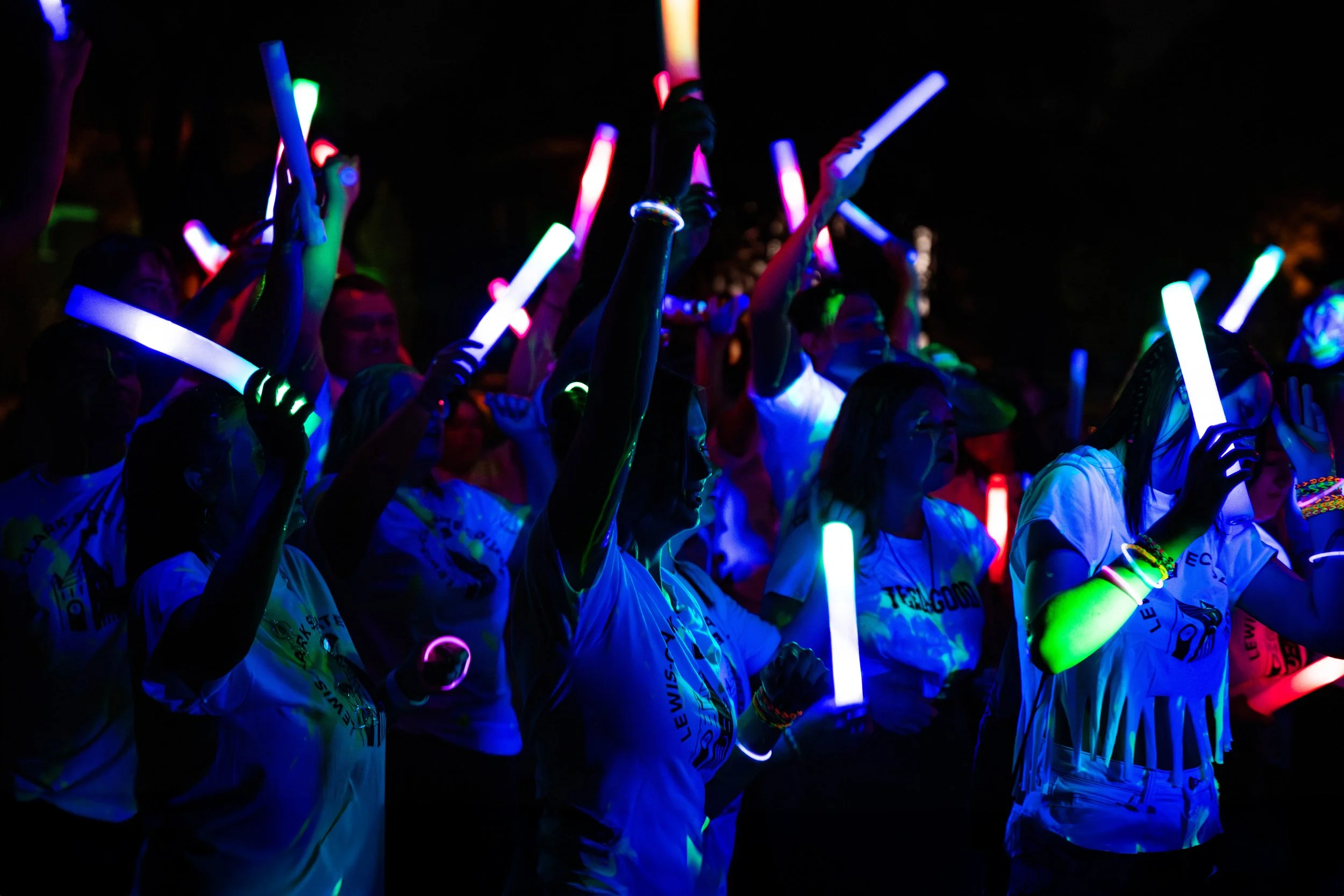 People at a night event holding colorful glow sticks.