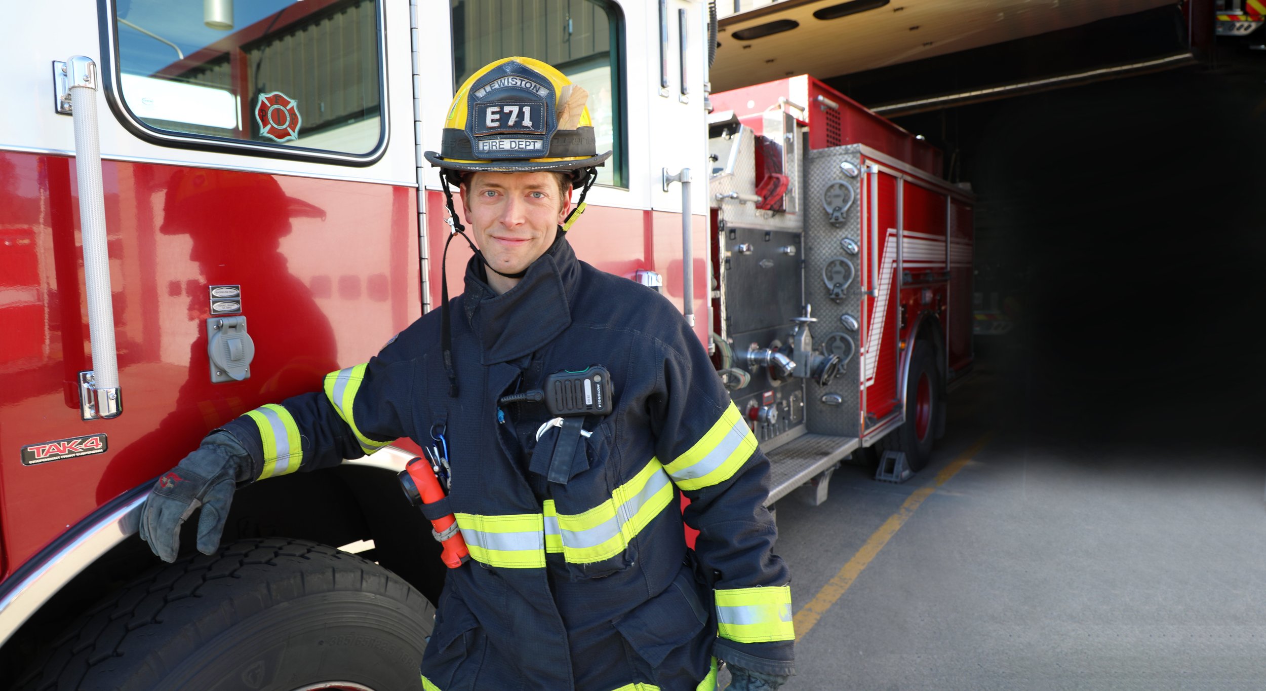 A firefighter in uniform and helmet standing next to a red fire truck.