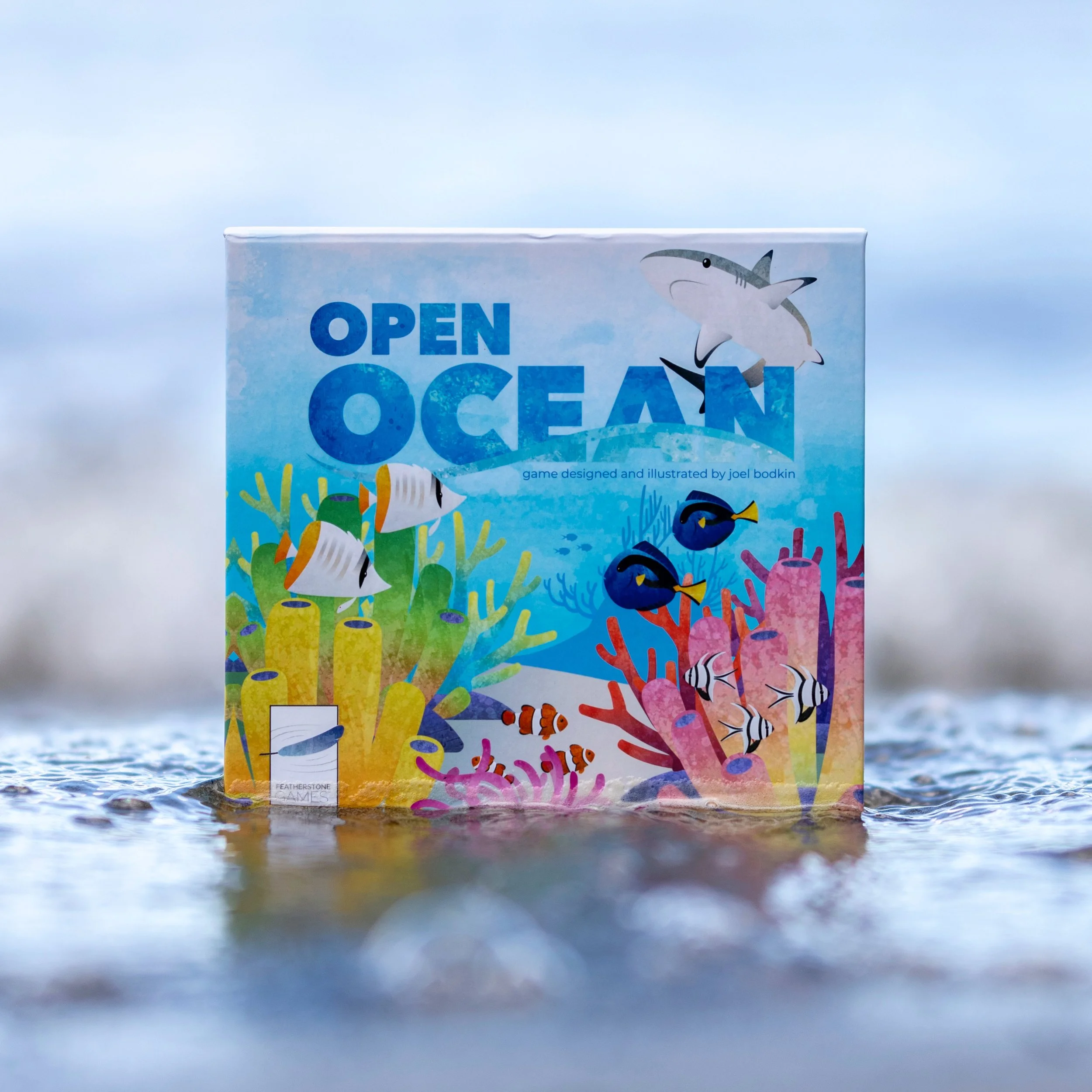 Box for the game 'Open Ocean' with illustrations of various sea creatures and coral, set on a wet surface.