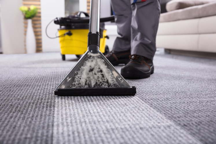 Professional cleaner using a carpet cleaning machine to deep clean residential carpet and remove stains and dirt.