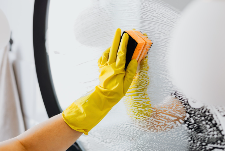 Gloved hand cleaning a glass mirror with a sponge for streak-free results and professional residential cleaning services.