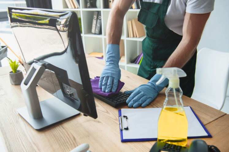 Professional cleaner disinfecting a computer keyboard on an office desk with supplies, highlighting commercial office cleaning services.