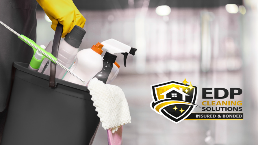 Gloved hand holding a bucket of professional cleaning supplies including spray bottles, cloths, and disinfectants for residential cleaning services.