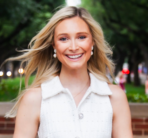 A young woman with blonde hair smiling outdoors.