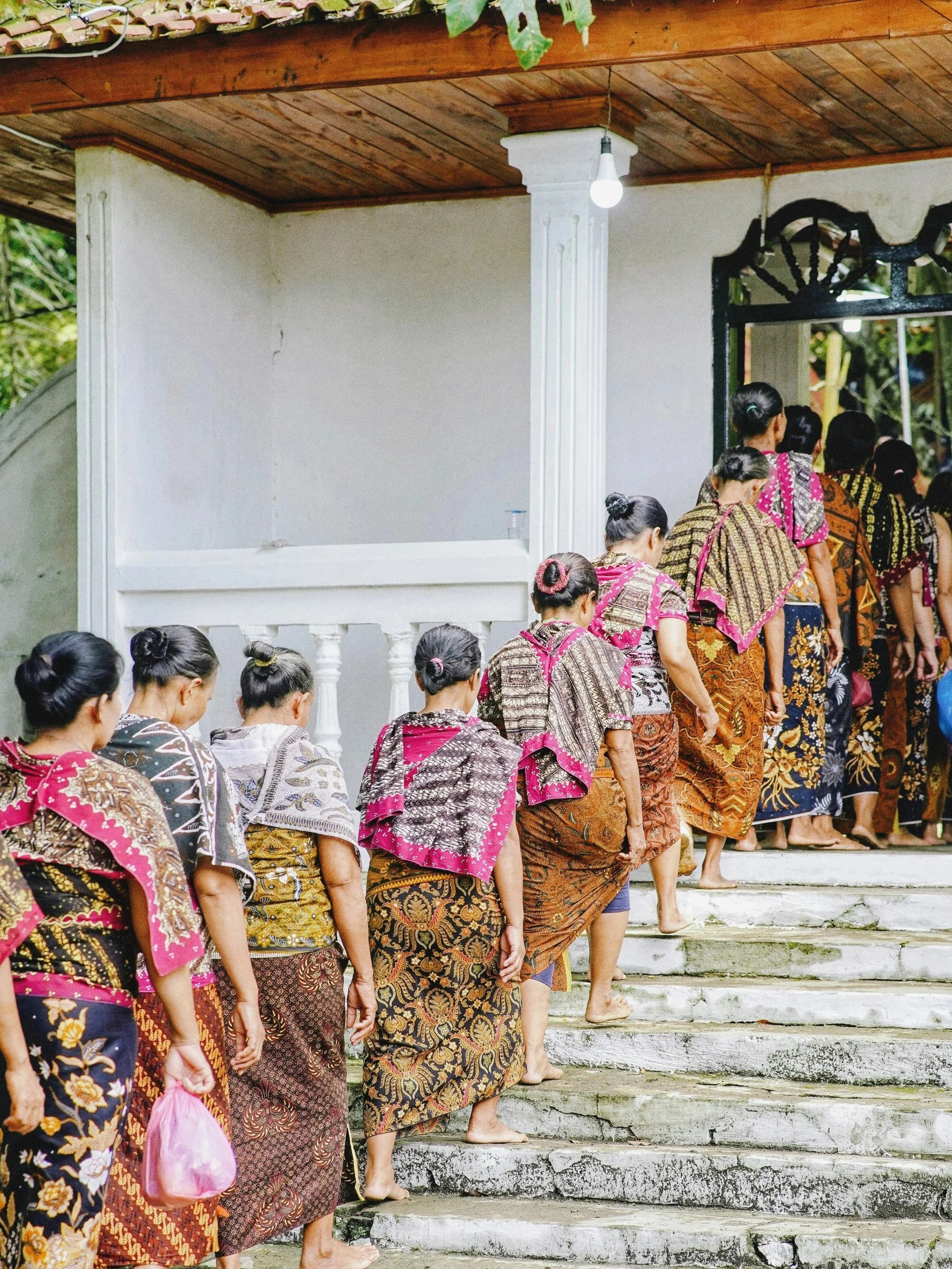 Women in traditional Javanese batik clothing and with tied-up hair are standing in line, walking up the worn, white stone steps to a building entrance - Premium Indonesian Green Coffee Beans Exporter