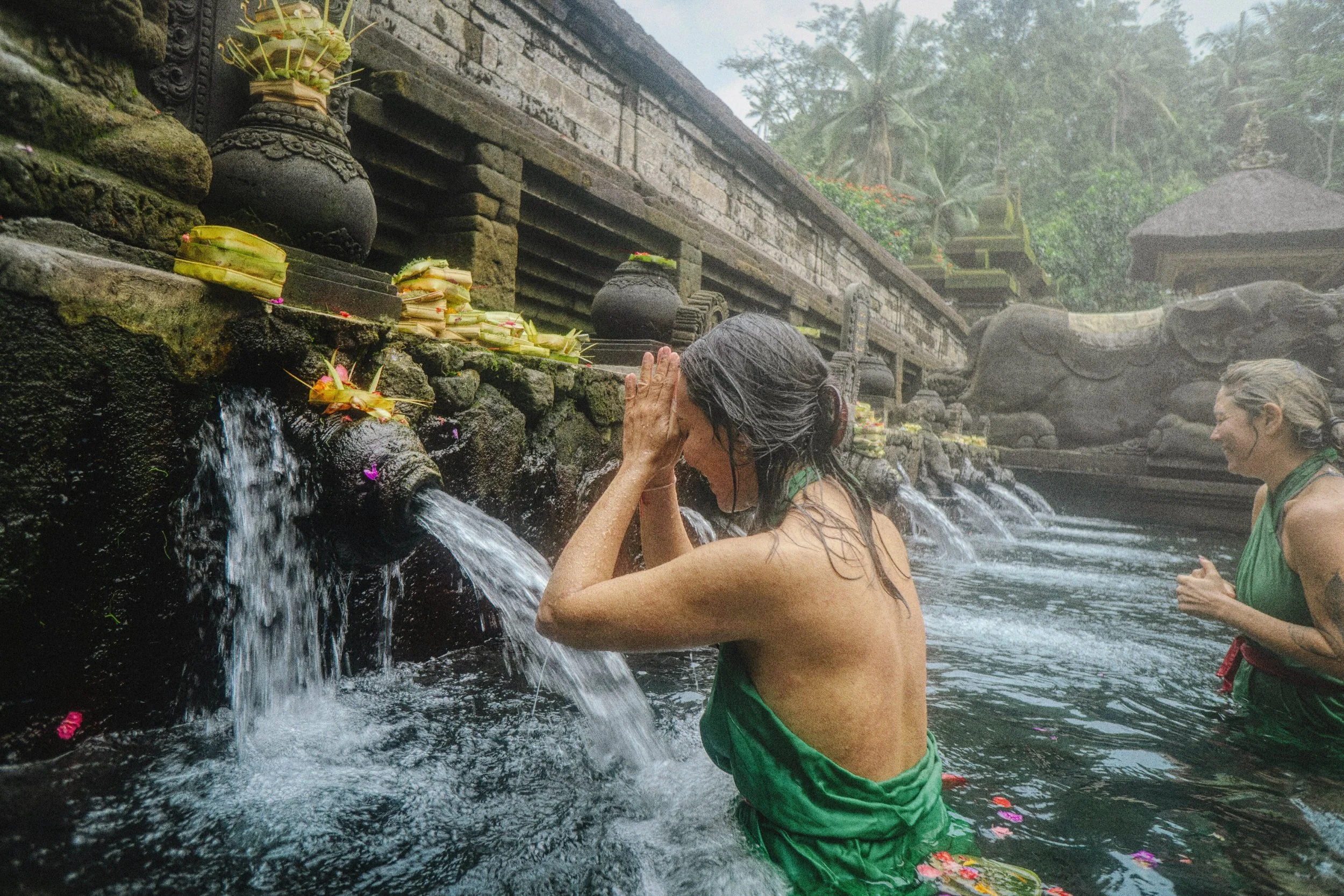 Two women in traditional green clothing participating in a water purification ritual at a sacred spring located in the island of Bali - Premium Indonesian Green Coffee Beans Exporter