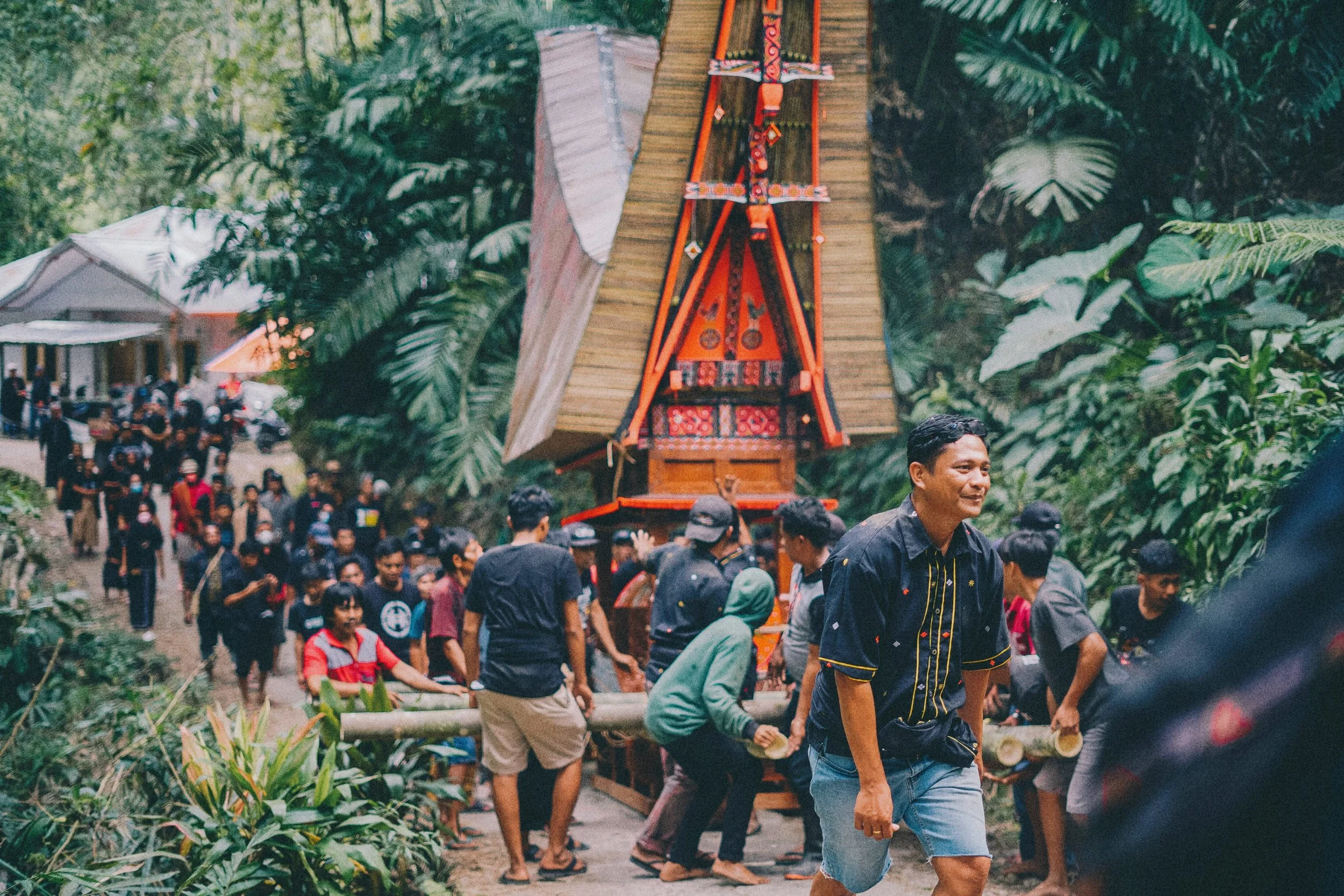 Group of people gathered outdoors around a traditional wooden structure, a cultural event, with lush green tropical foliage in the background located in Sulawesi - Premium Indonesian Green Coffee Beans Exporter