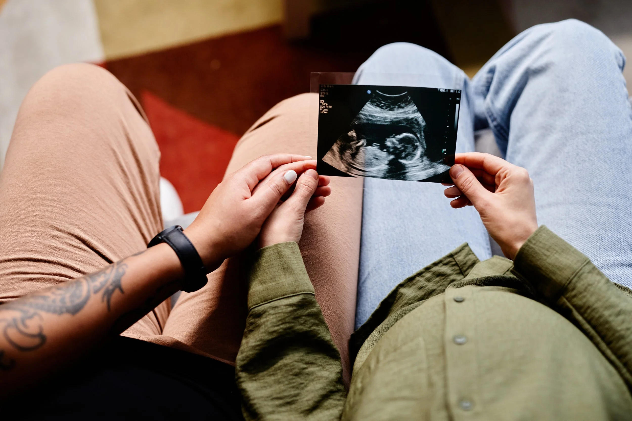Person holding an ultrasound image of a developing fetus, sitting on a person's lap.