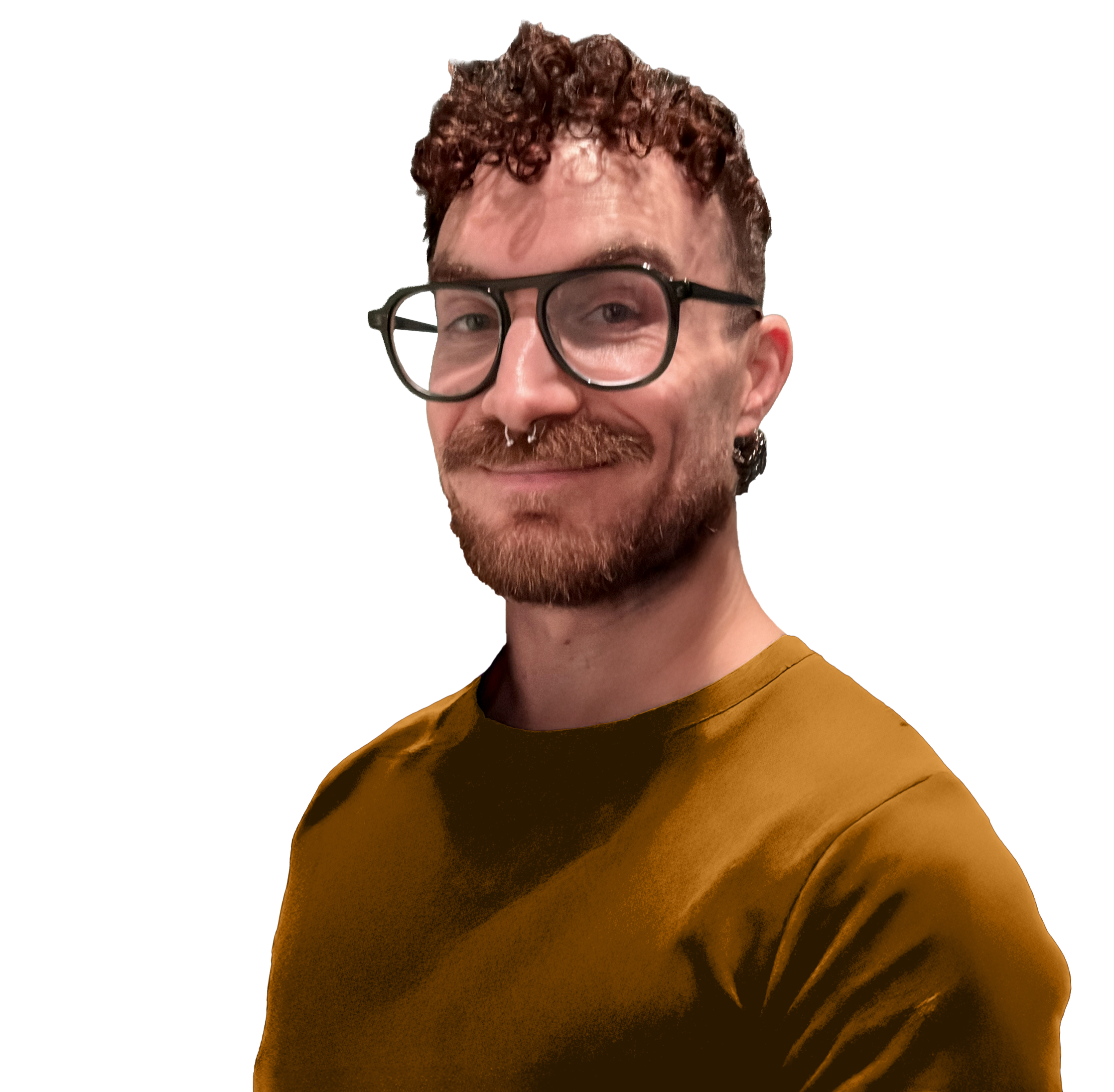 A man with curly brown hair, glasses, a septum piercing, a nose ring, and a beard, wearing a mustard-colored shirt, smiling.