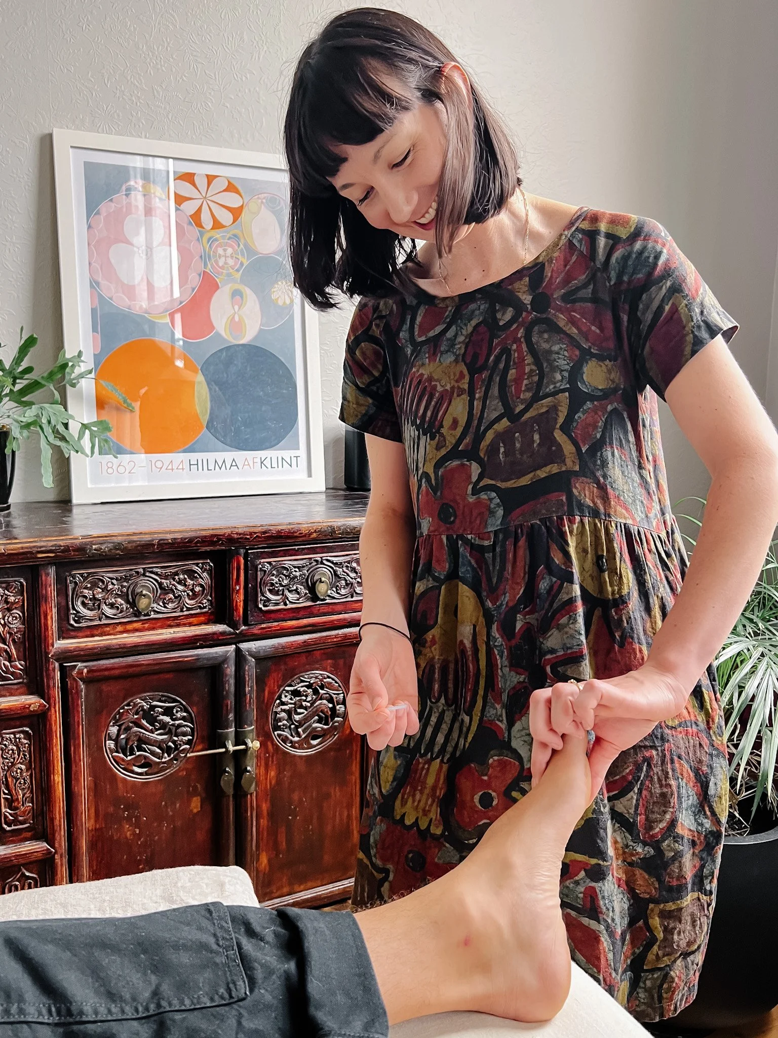 Smiling acupuncturist inserting an acupuncture needle into the foot
