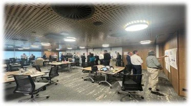 Collaboration meeting in a modern conference room with multiple desks, chairs, and people working.