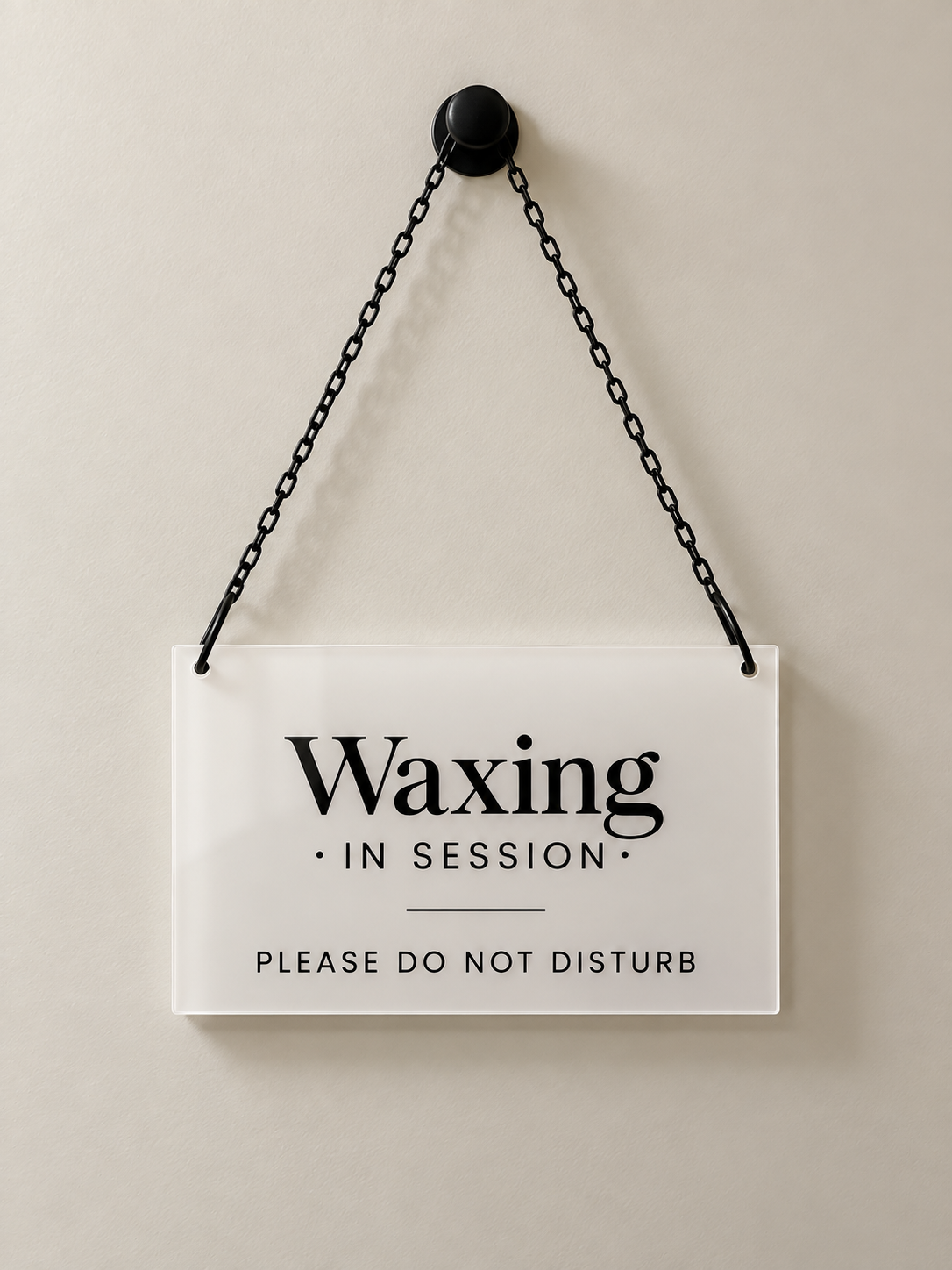 A white sign hanging from a black chain reads 'Waxing in Session. Please do not disturb.' on a plain, light-colored wall.