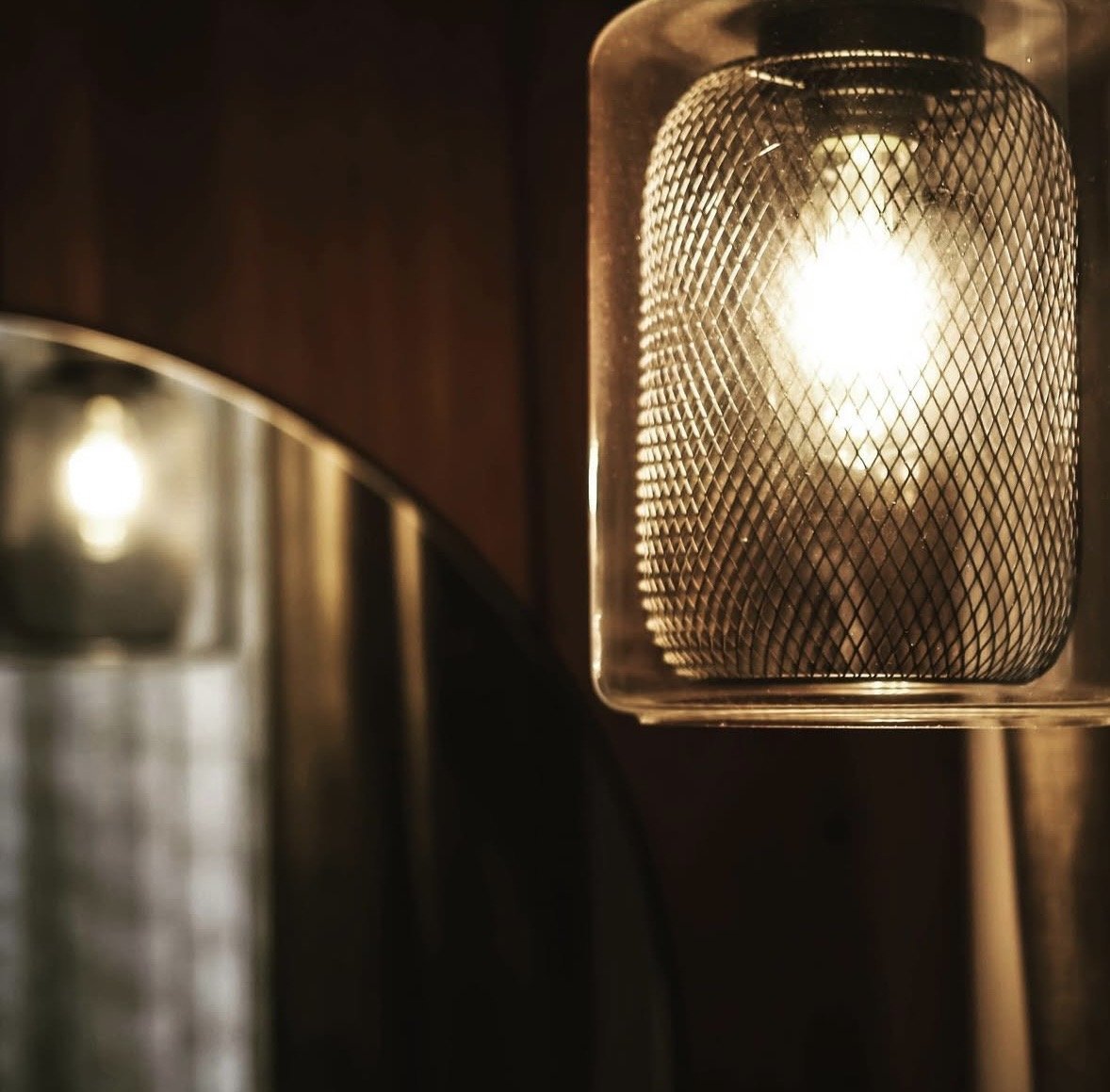 Close-up of a warm-colored industrial-style wall sconce with a wire mesh cover, emitting a warm glow in a dimly lit interior.