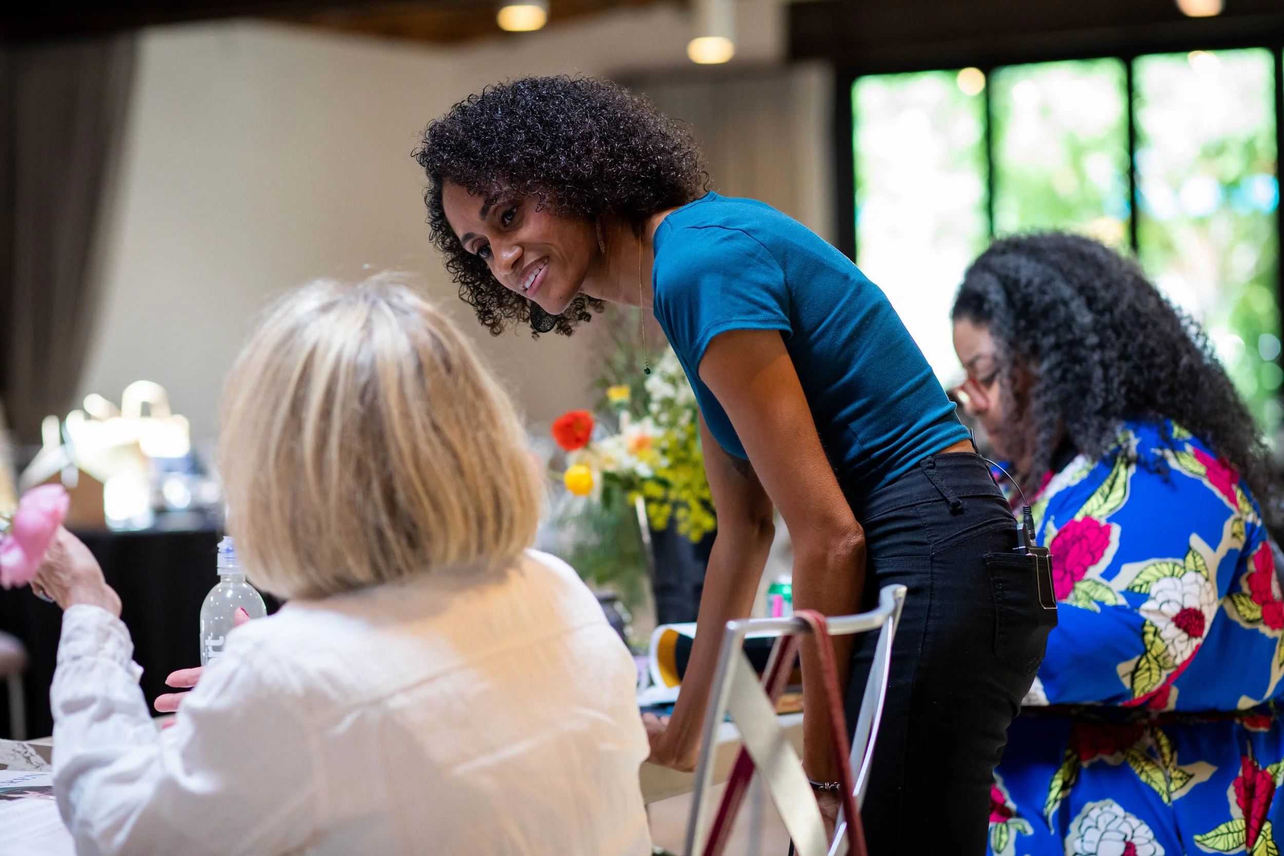 Photo of Crystal, a Black woman with shoulder length dark brown curly hair, leaning over a table to speak to a workshop participant