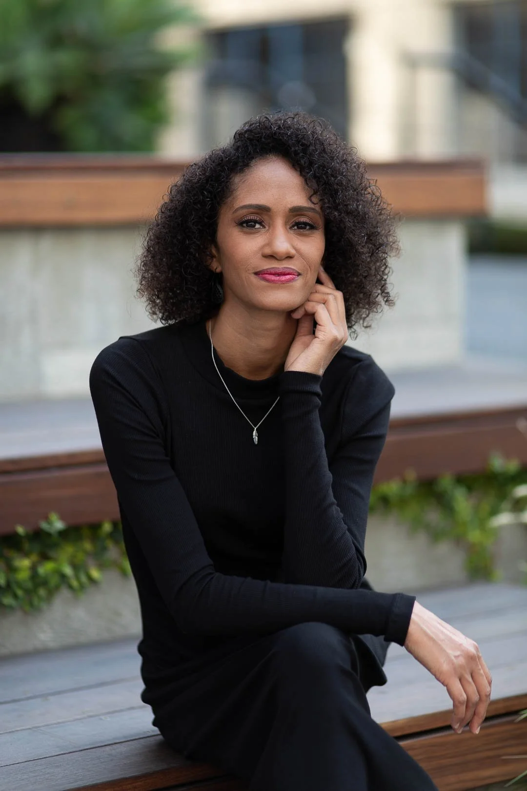 Photo of Crystal, a Black woman with shoulder length curly hair, sitting on a wooden bench, smiling softly at the camera