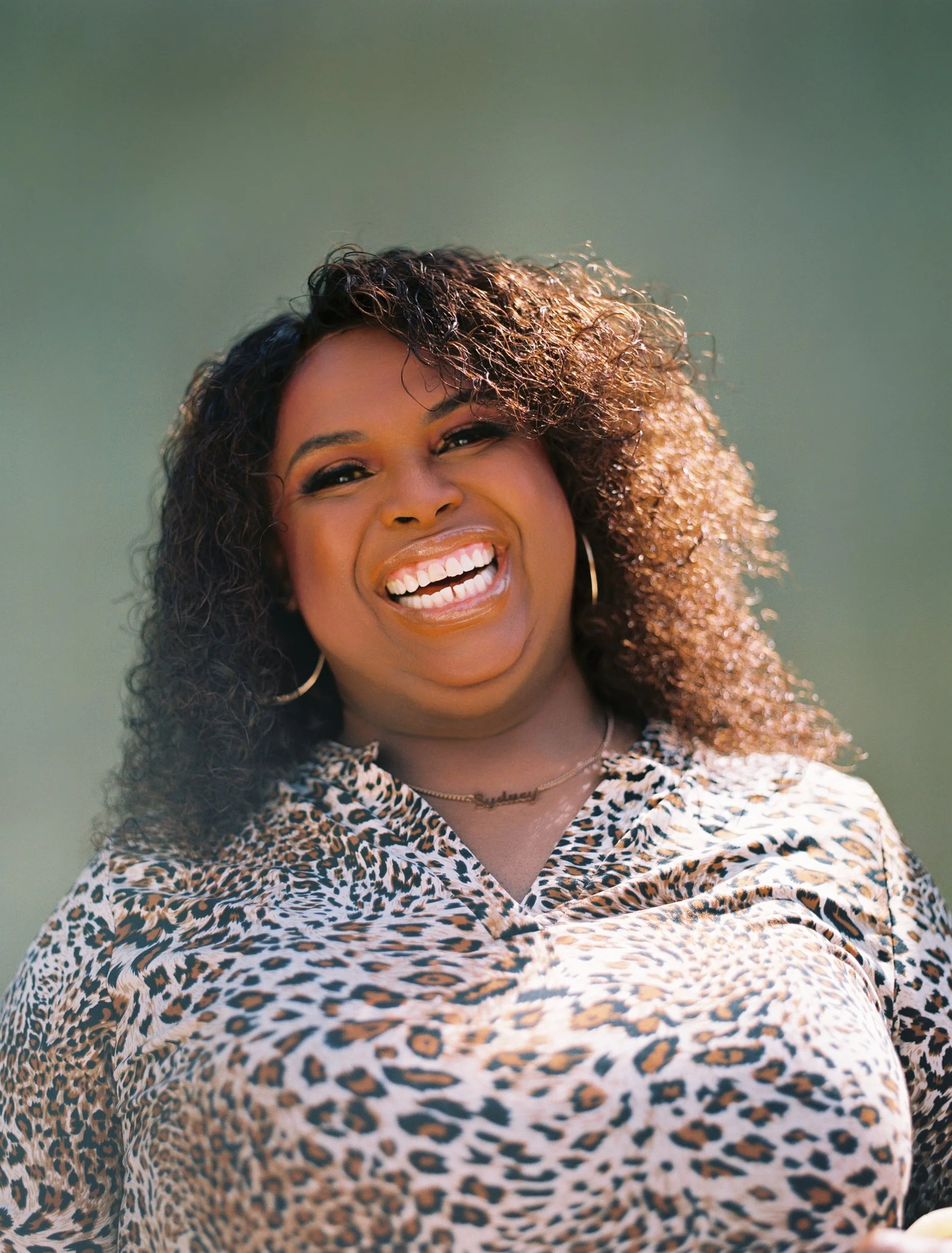 Headshot of a Black woman with shoulder length curly hair, smiling brightly at the camera