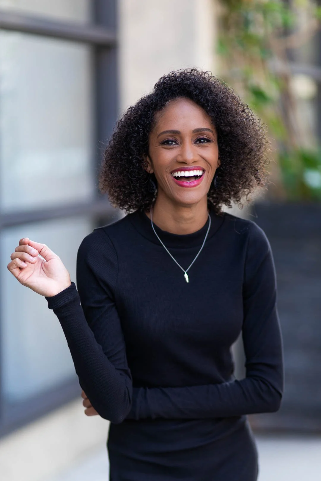 Photo of Crystal, a Black woman with shoulder length curly hair, standing, wearing a black dress, laughing into the camera