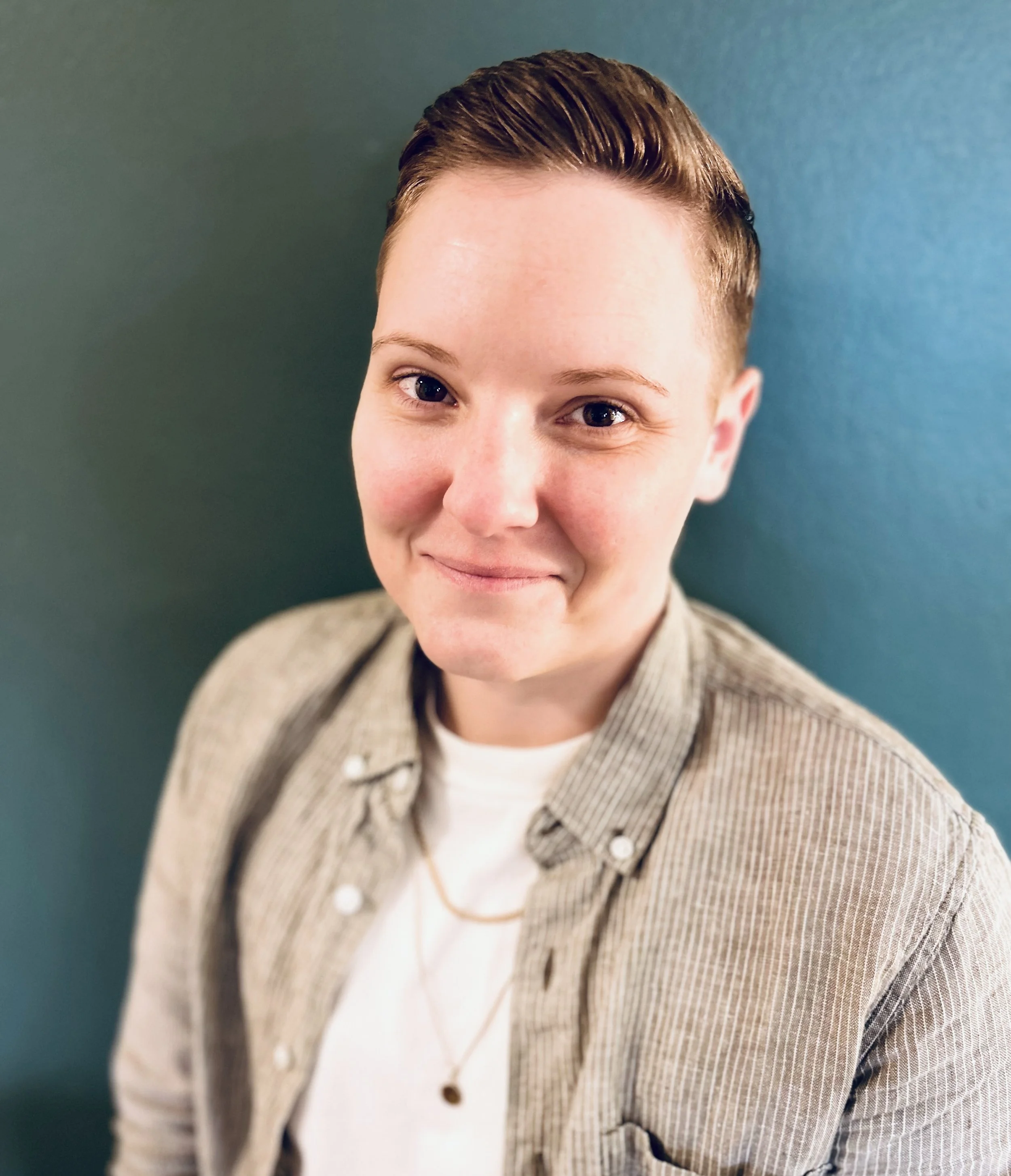Headshot of a white, nonbinary person, smiling at the camera