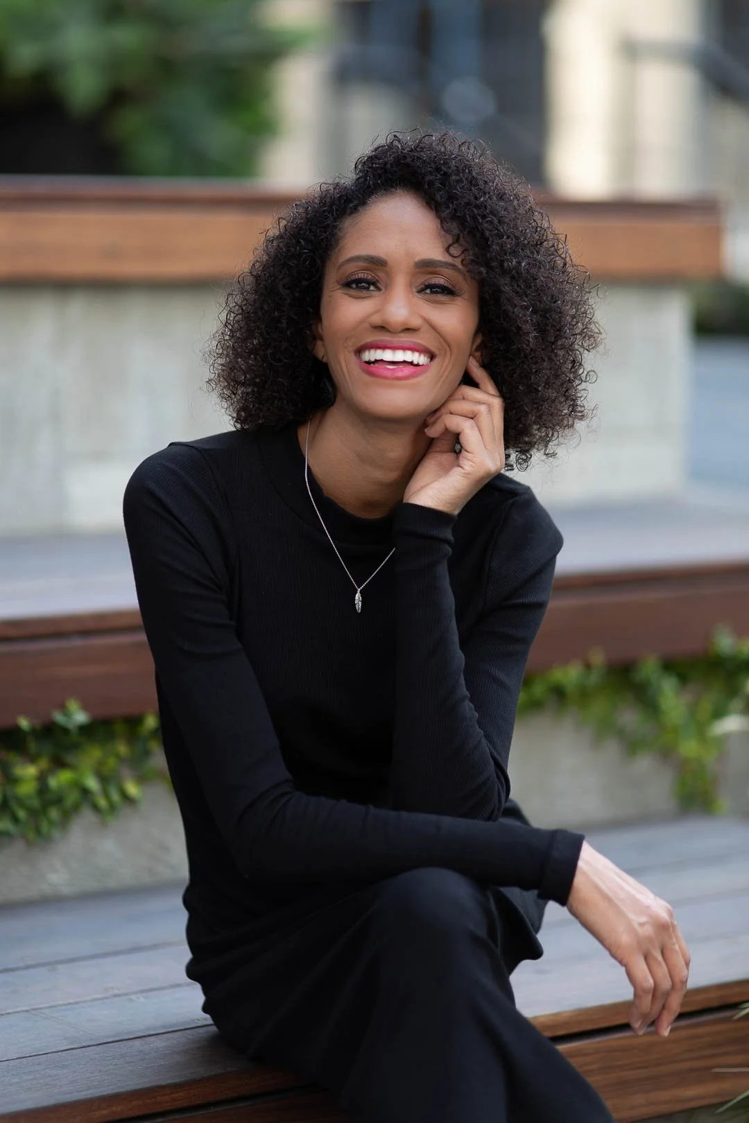 Photo of Crystal, a Black woman with shoulder length curly hair, sitting on a wooden bench, smiling at the camera
