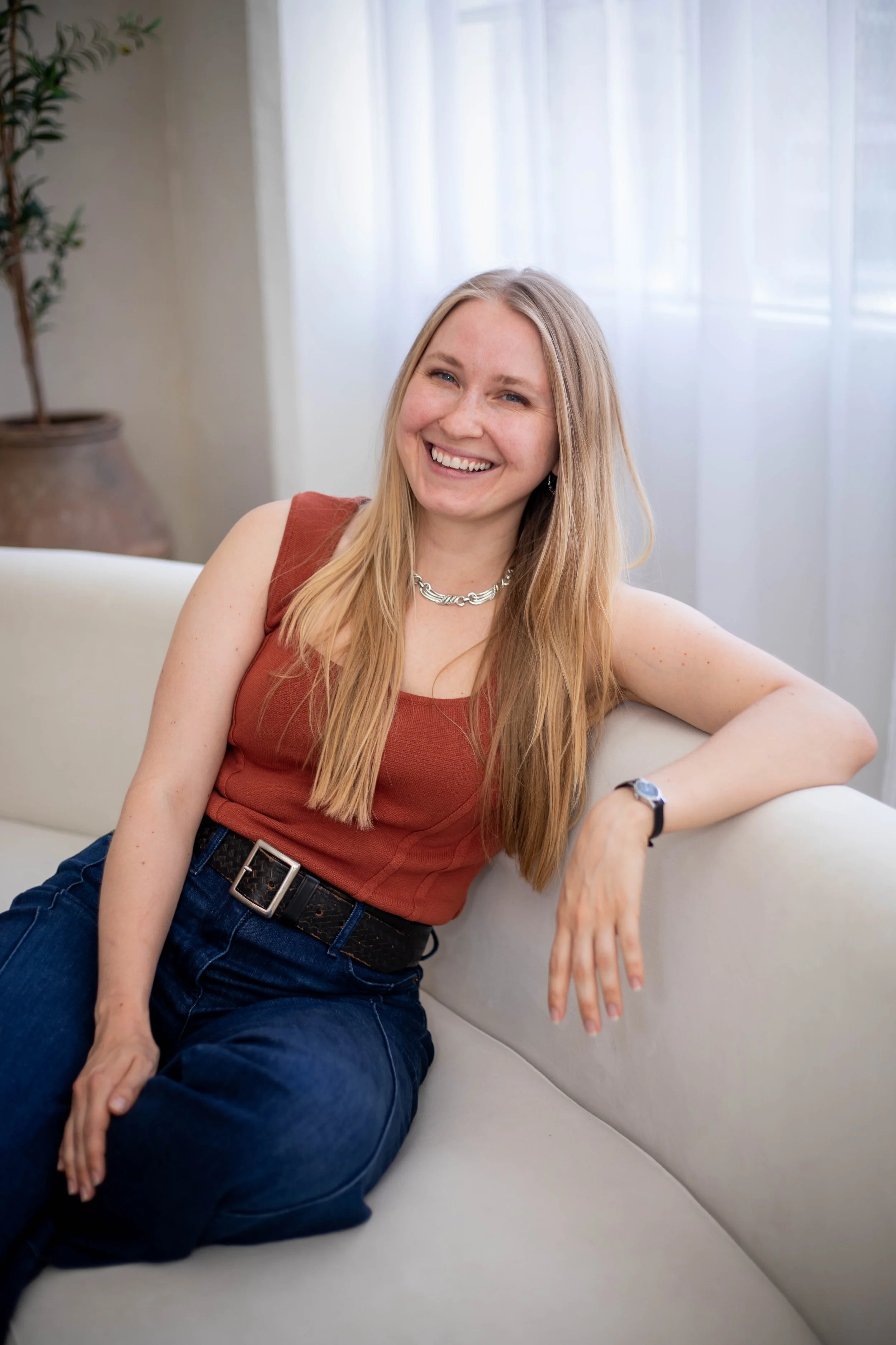 Photo of a white woman with long blonde hair, sitting on a couch, smiling at the camera