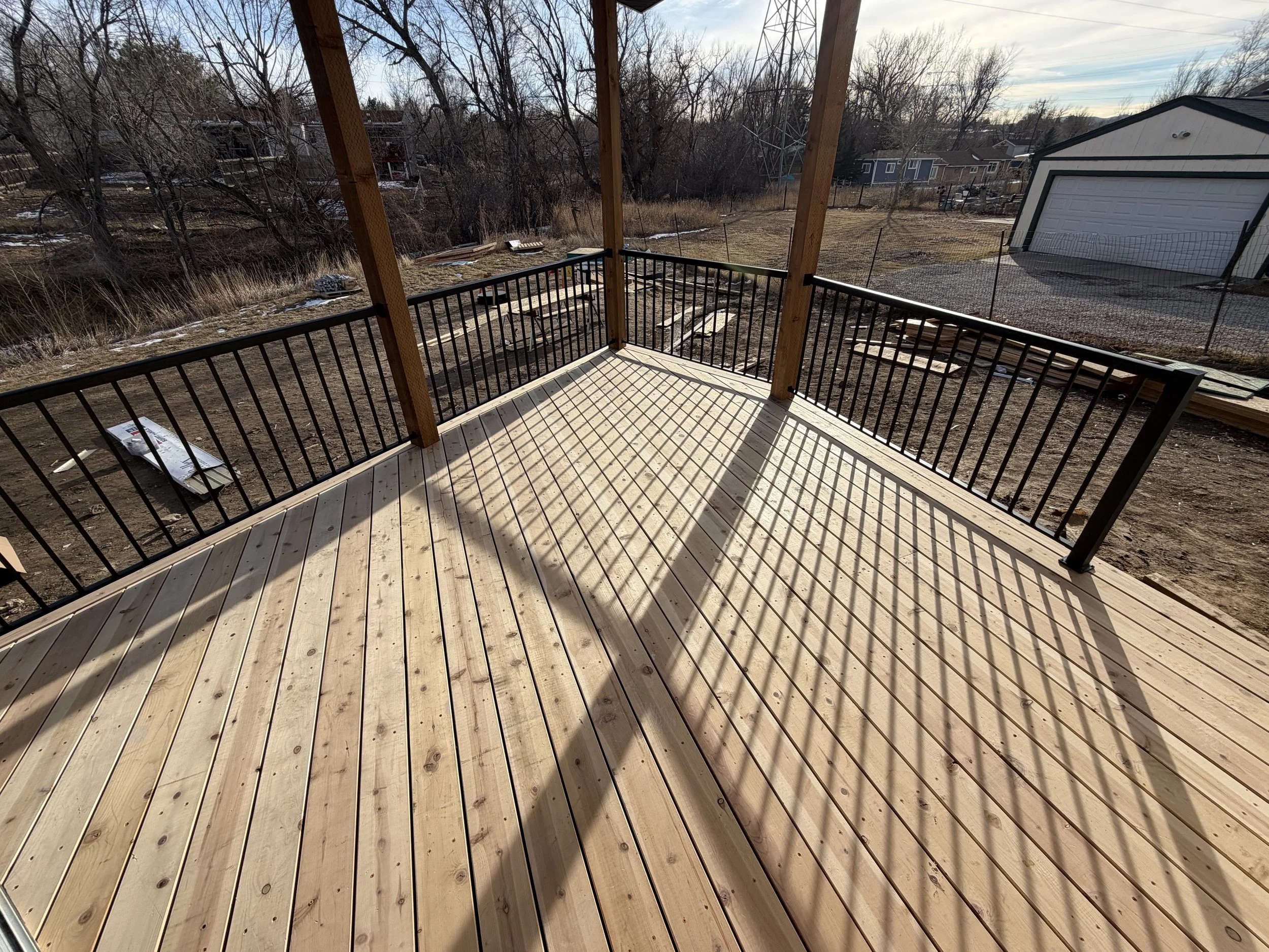 Wooden deck with black metal railing, attached to a house, overlooking a backyard with bare trees, grass, and a shed in the distance.