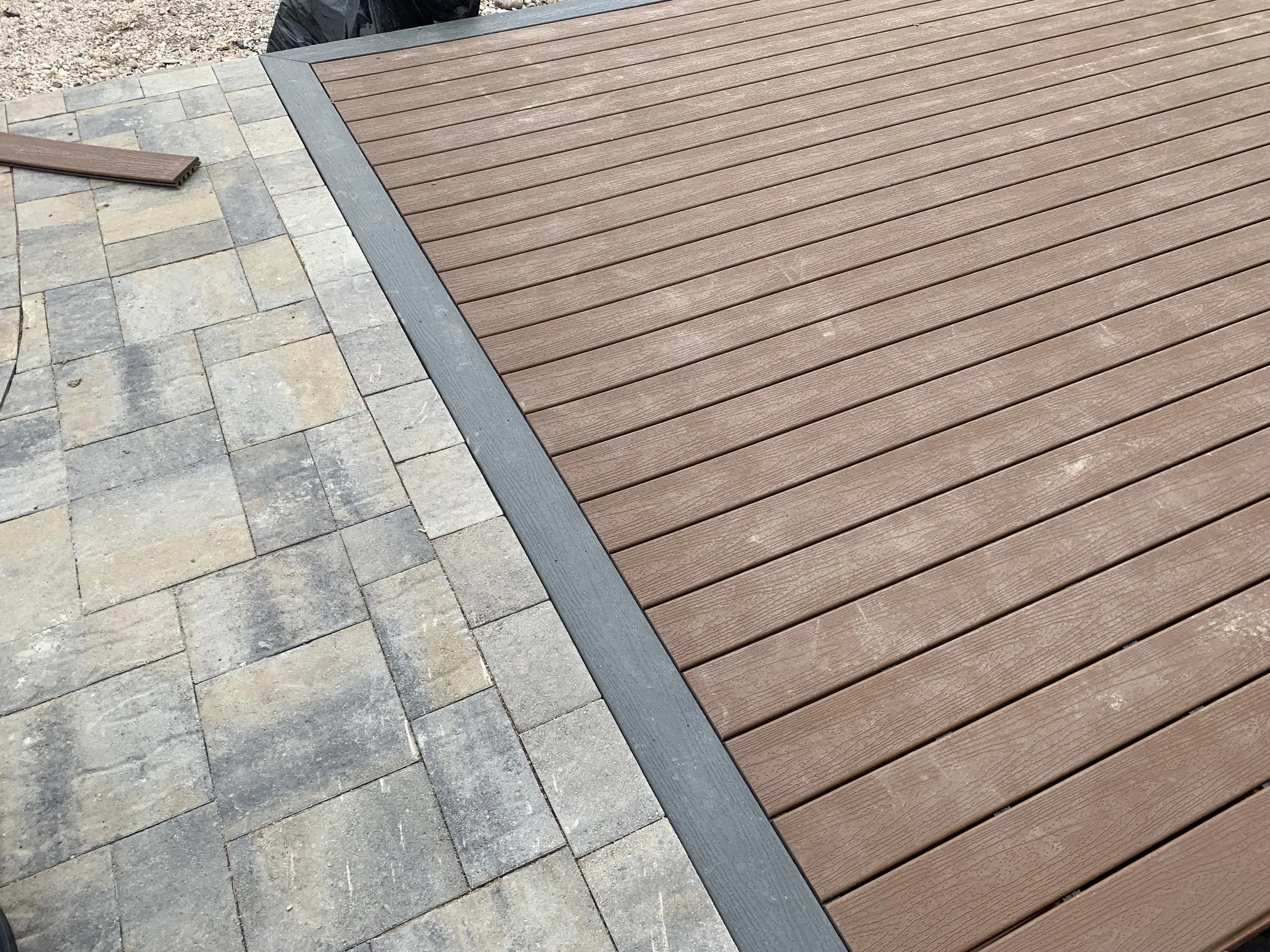 Close-up of a patio with gray stone pavers and a redwood deck edged with a black border.