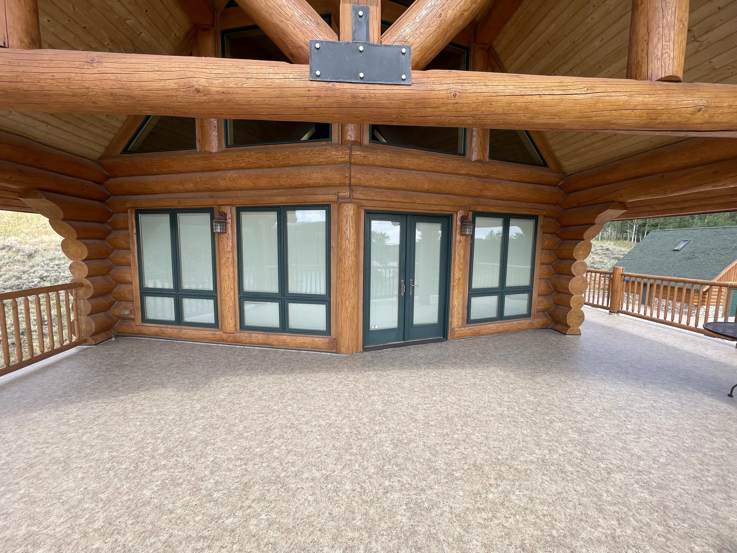 A spacious balcony with a beige carpet, wooden walls and railing, and glass doors leading into a log cabin-style interior.